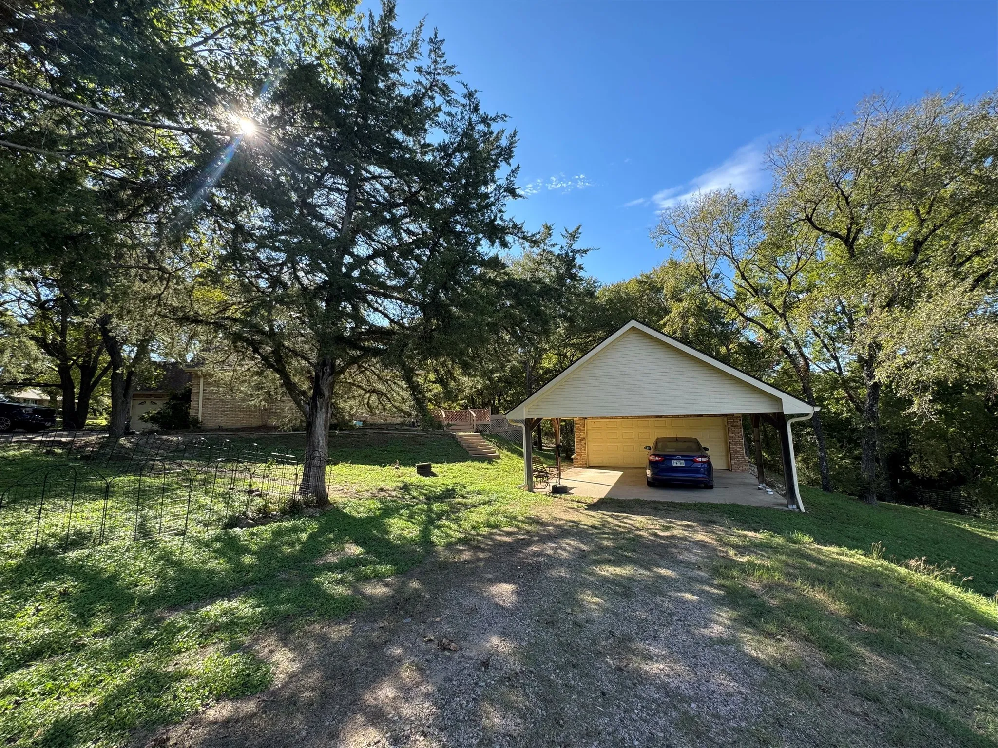 Detached carport structure with a gabled roof, gravel driveway, and mature trees
