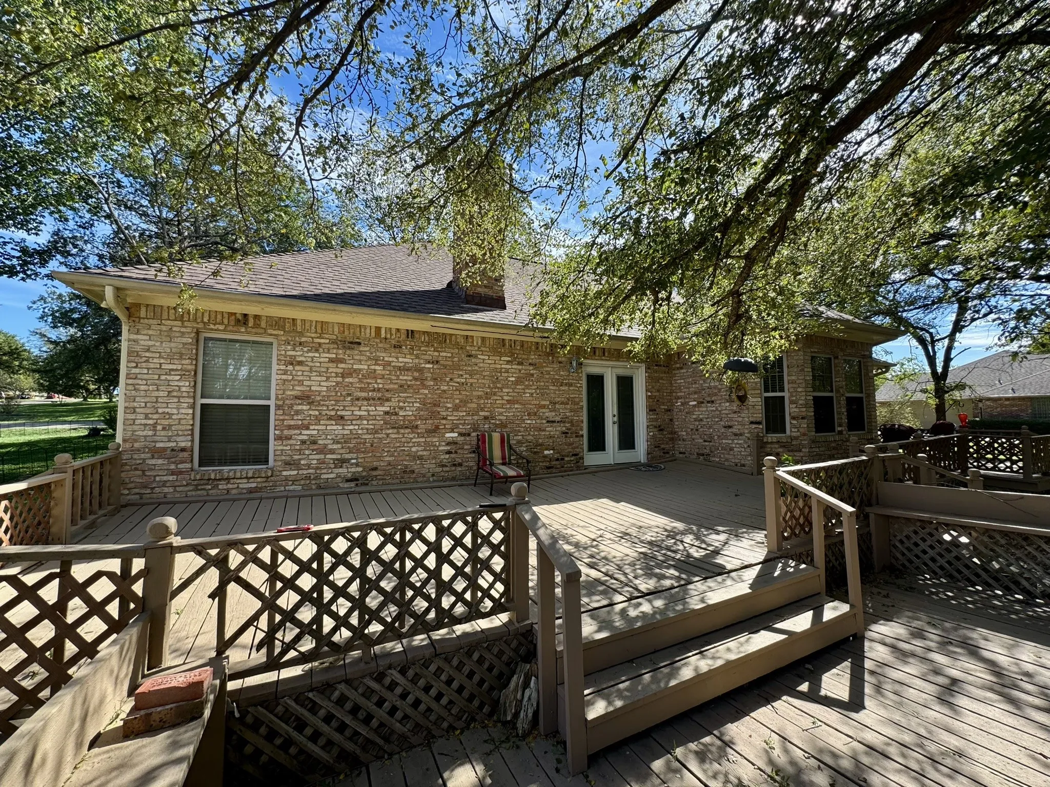 Multi-level wood deck featuring lattice railing, brick exterior, chimney, and glass-paneled double doors