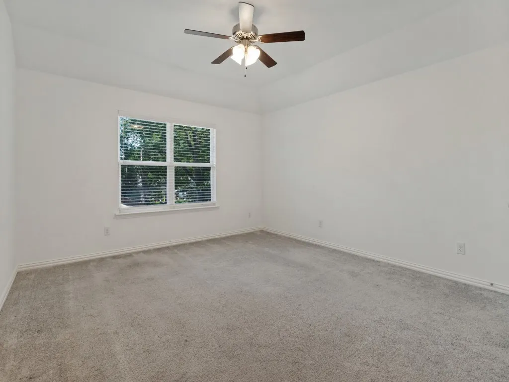 Comfortable bedroom featuring soft carpeting, a ceiling fan, and natural light.