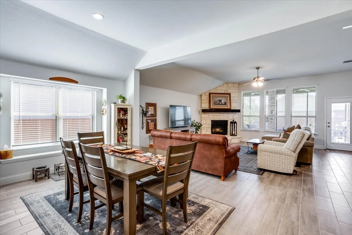 Open-concept interior featuring vaulted ceilings, wood-finish tile flooring, stone-faced fireplace with a wood mantel, and expansive windows