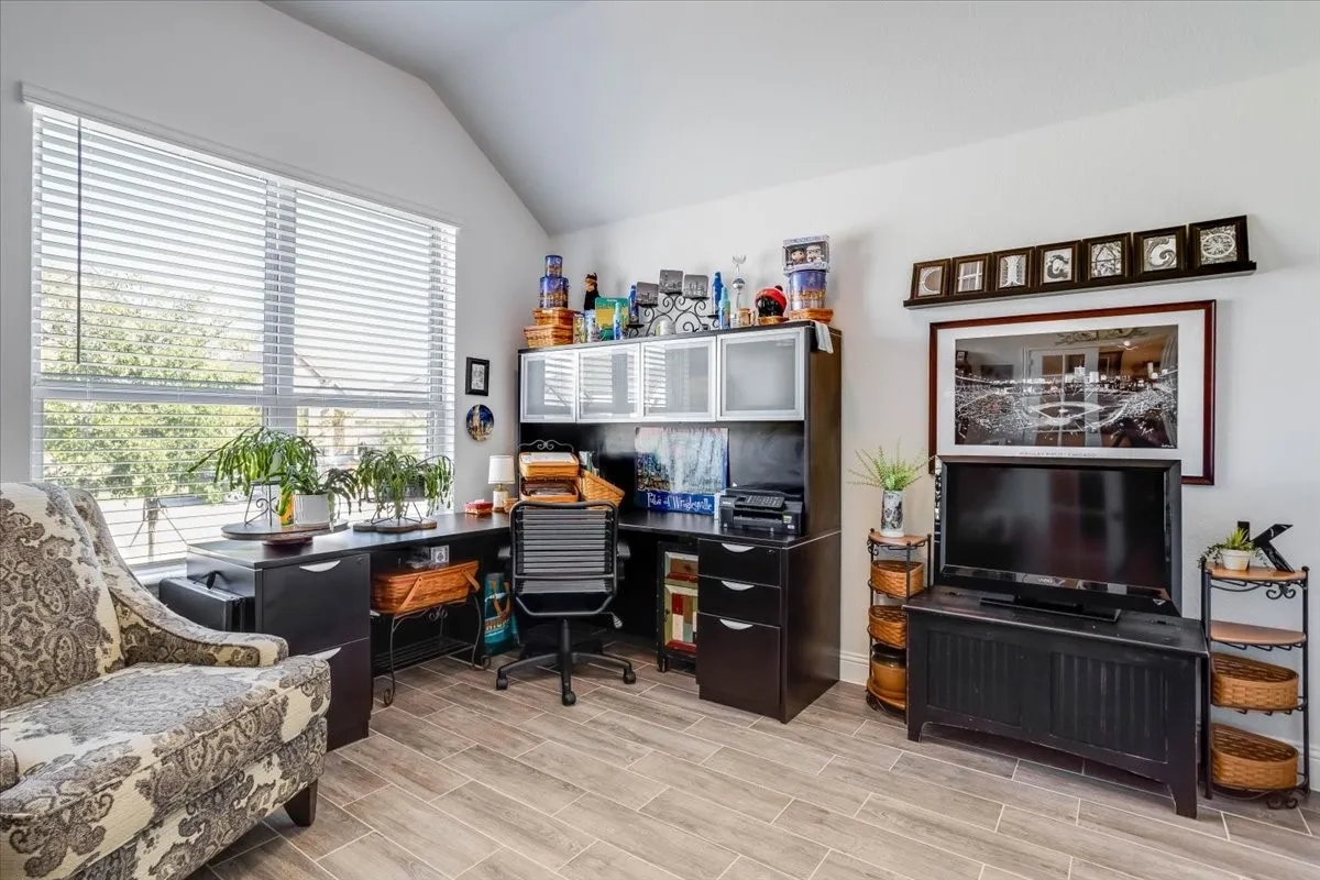 Vaulted ceiling, large window with adjustable horizontal blinds, and wood-finish tile flooring