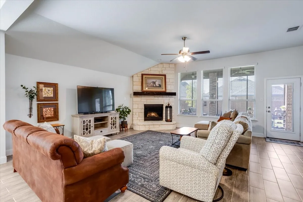 Living area featuring wood-finish tile flooring, vaulted ceilings, and a corner stone-clad fireplace with a prominent wooden mantel