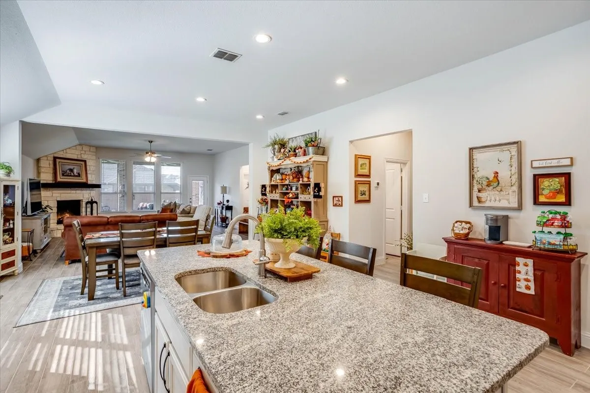 Kitchen island featuring a stone countertop, undermount double-basin stainless steel sink, and high-arc faucet, complemented by wood-finish flooring and recessed lighting