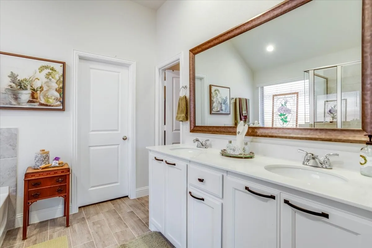 Double vanity featuring white cabinetry, a solid-surface countertop, dual undermount sinks, and a large wall-mounted mirror with a metallic frame