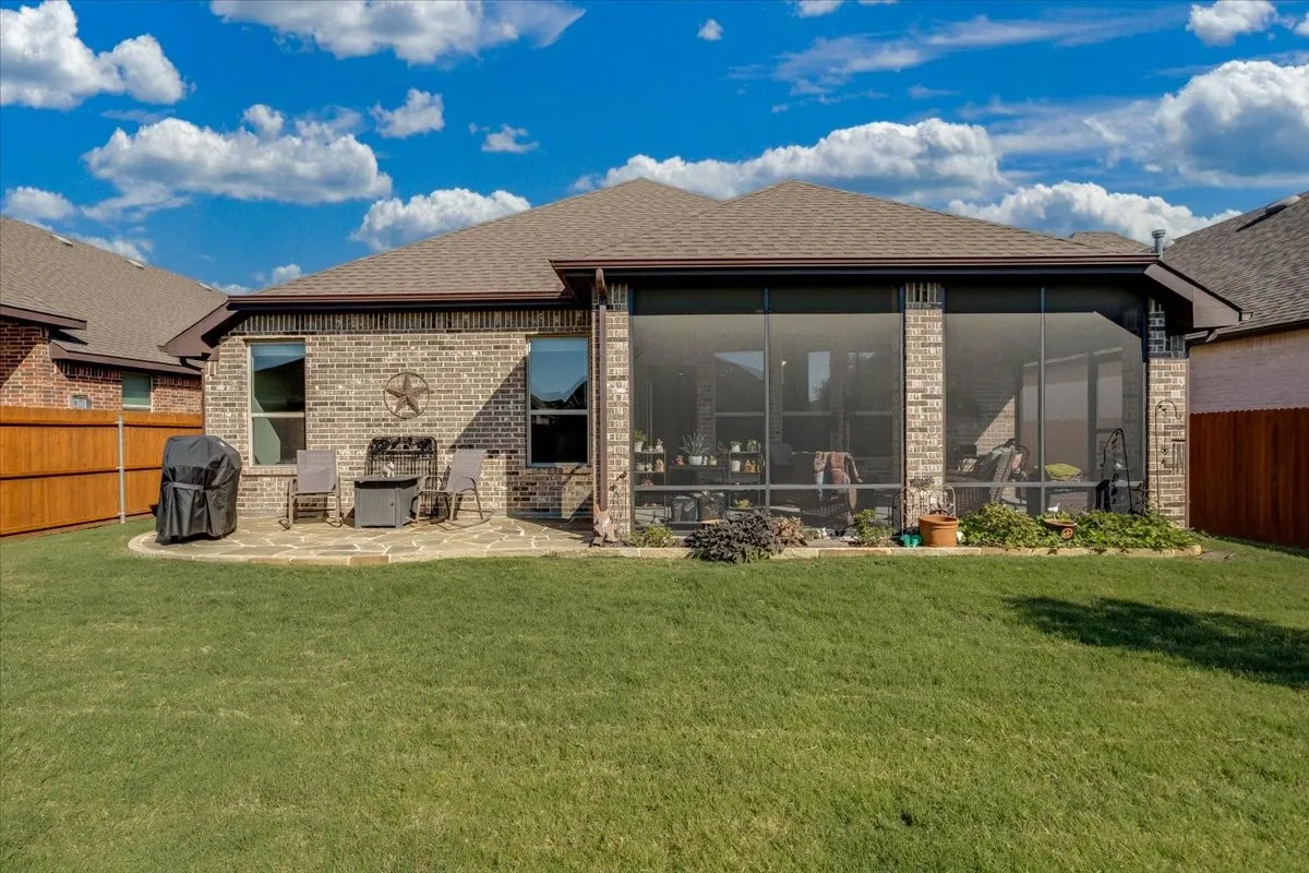 Brick exterior featuring a screened-in patio, natural stone hardscaping, and a wood privacy fence