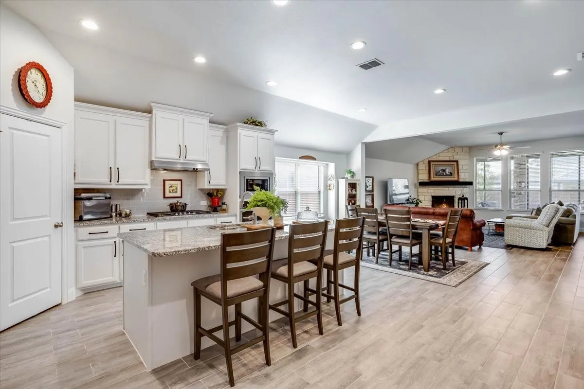 Kitchen featuring white cabinetry, stone countertops, a center island with bar seating, recessed lighting, and wood-finish tile flooring