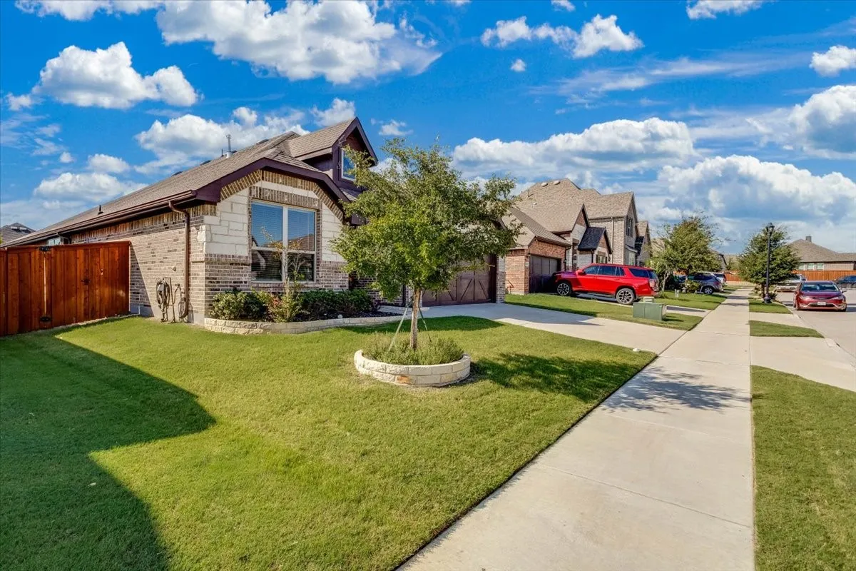 Exterior featuring brick and stone masonry, multi-gabled roofline, concrete driveway, and a front yard with a stone-bordered tree planter