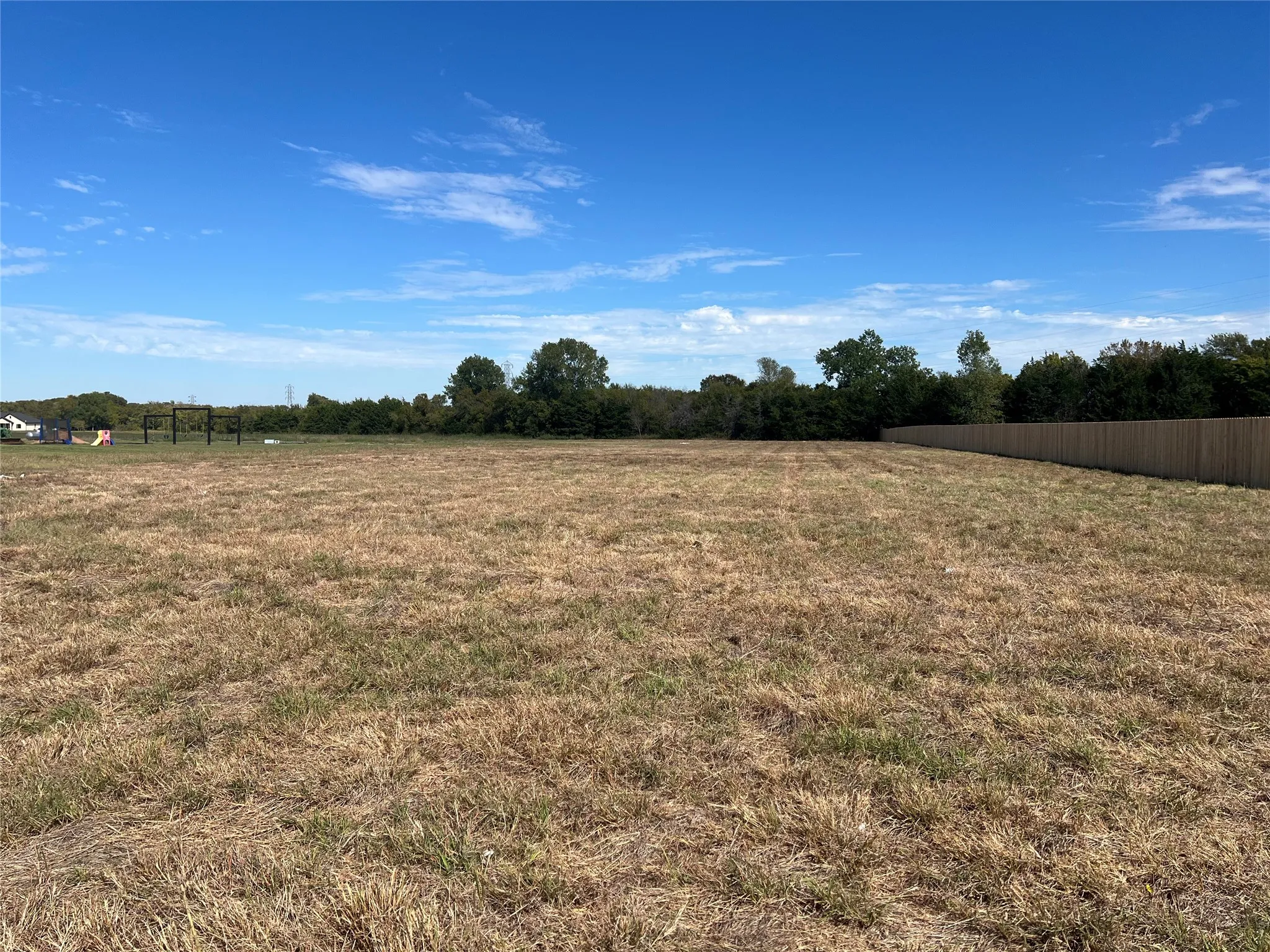 Expansive open lot featuring flat topography, a wood privacy fence, and mature perimeter trees