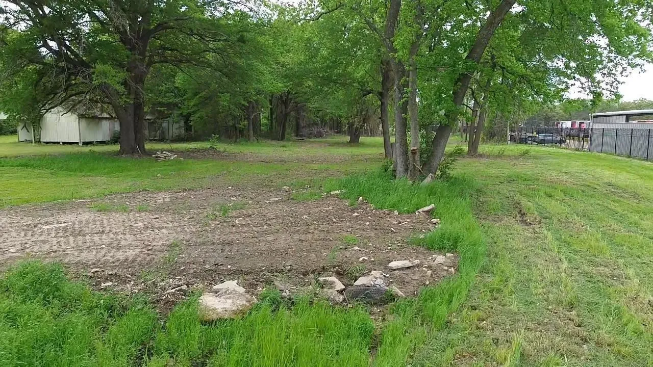 Expansive lot featuring mature trees, natural terrain, and a chain-link perimeter fence