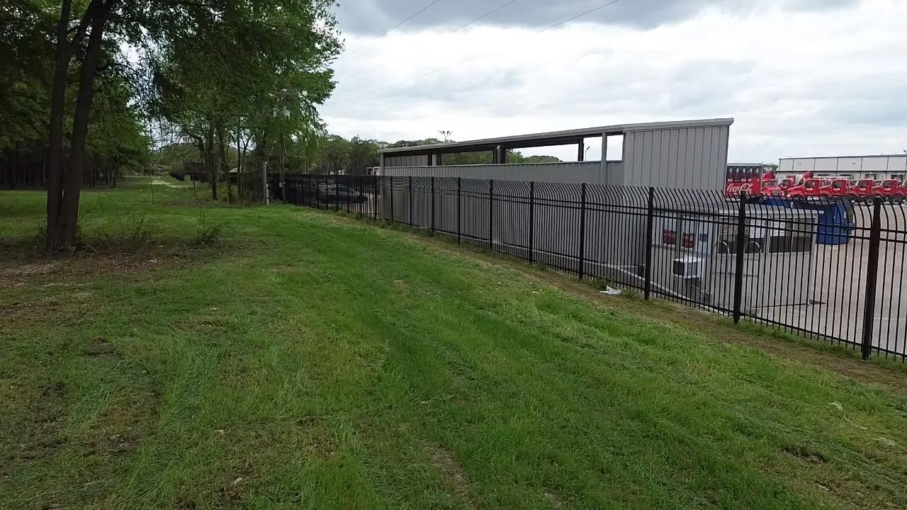 Level green space featuring established trees and perimeter metal fencing