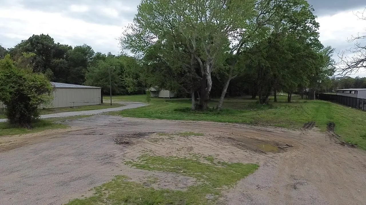 Expansive level lot featuring a metal-sided outbuilding, a gravel driveway, and mature trees