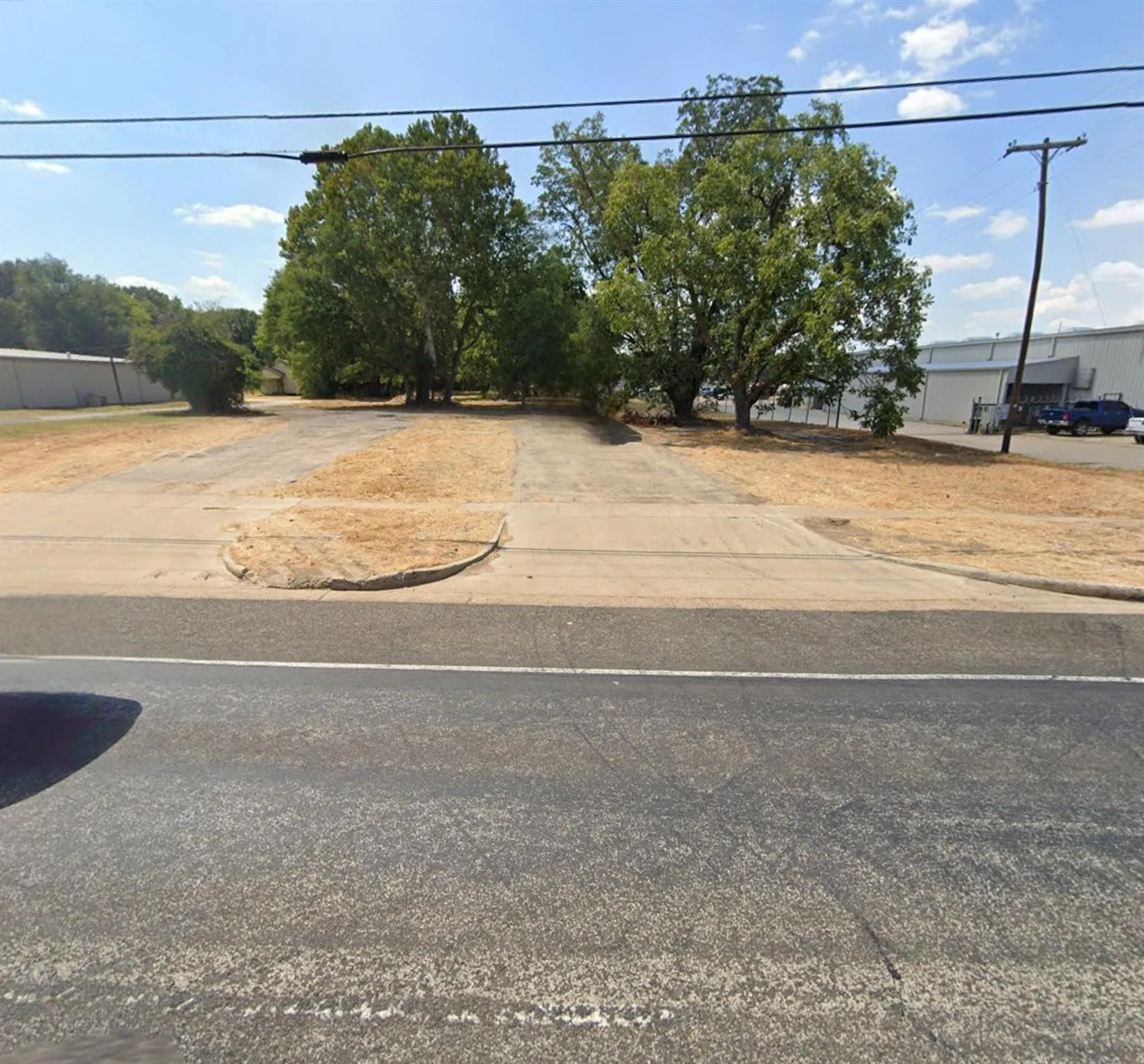 Level lot featuring asphalt paving, concrete curb cuts, and mature trees
