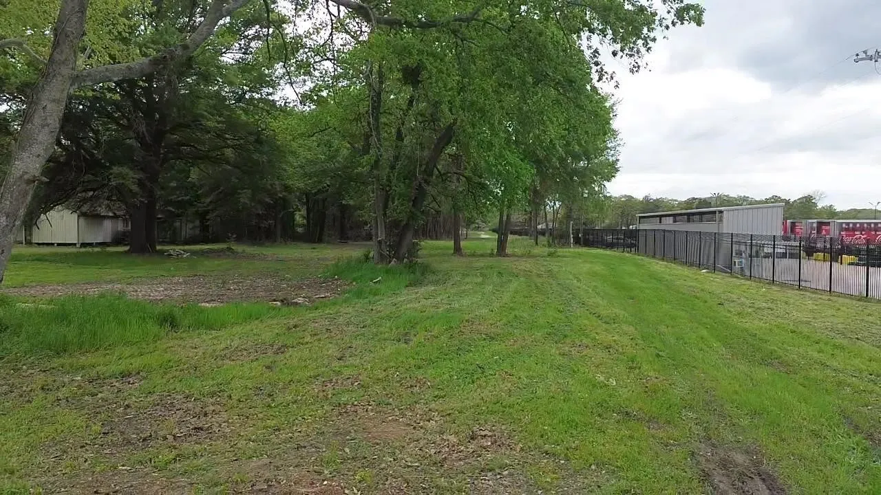 Expansive lot featuring mature hardwood trees and perimeter metal fencing