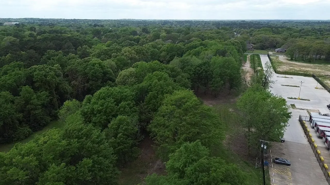 Aerial perspective of a sprawling lot featuring mature tree canopy, dense woodlands, and paved surface parking