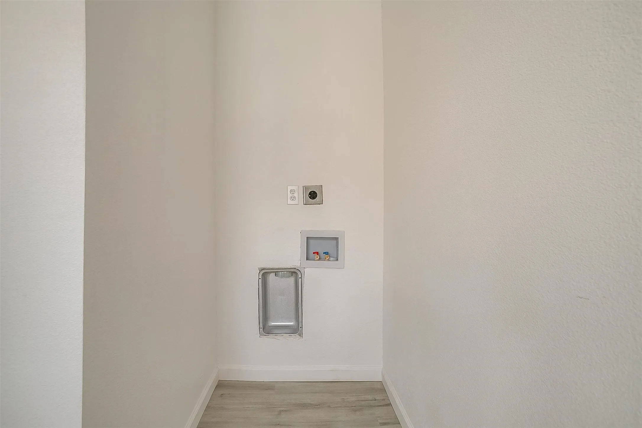 Laundry area featuring recessed plumbing connections, a dedicated dryer vent, and light-toned wood-finish flooring