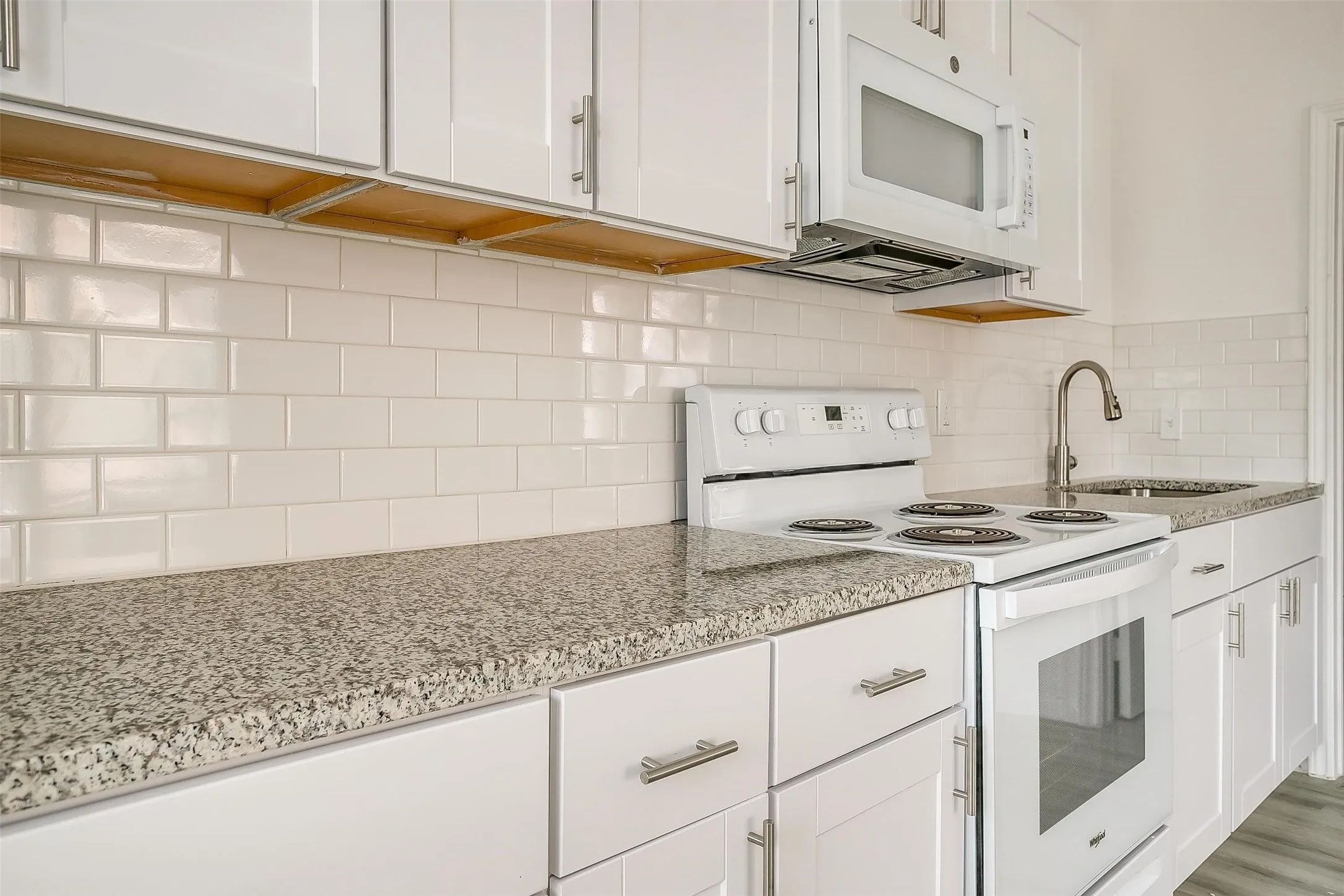 Kitchen featuring white Shaker-style cabinetry, stone-finish countertops, subway tile backsplash, and stainless steel hardware
