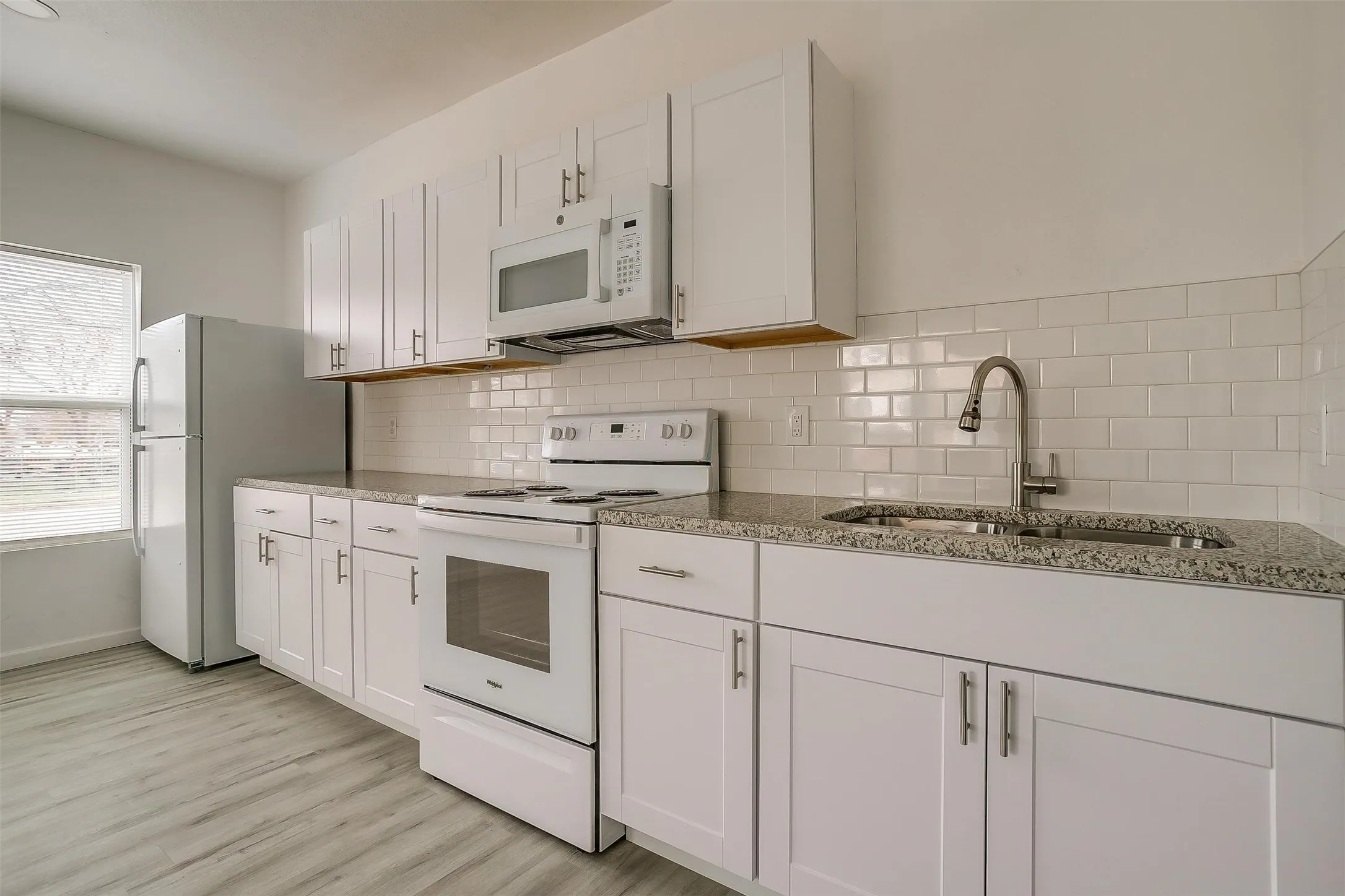 Kitchen featuring white shaker-style cabinetry, stone-finish countertops, white subway tile backsplash, and light-tone wood-finish flooring