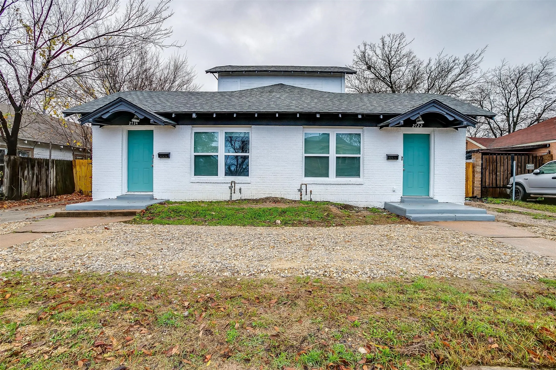 White-painted brick exterior featuring twin entryways with peaked gable accents, teal front doors, and dual concrete stoops