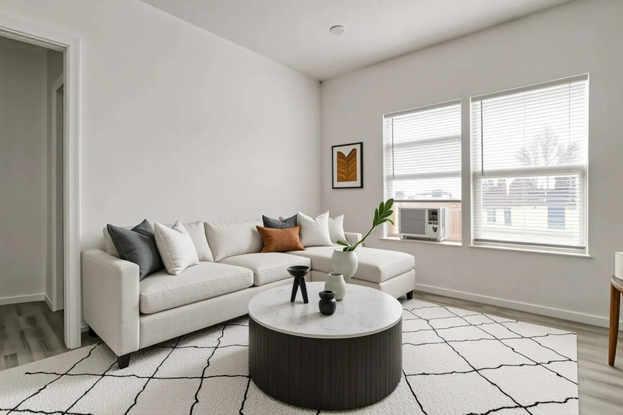 Neutral-toned interior space featuring light-colored walls, wood-finish flooring, and two windows with horizontal blinds