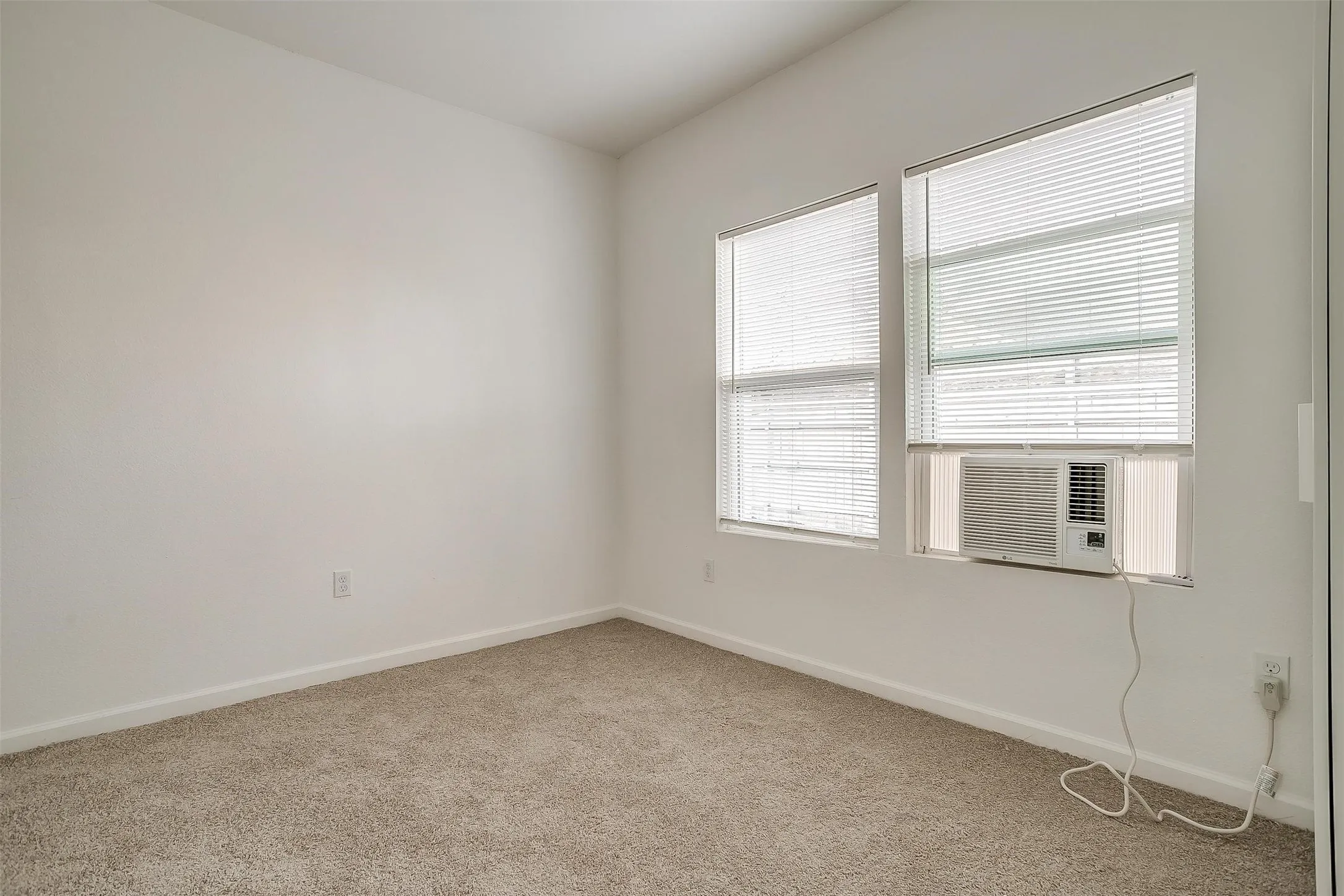 Neutral-toned wall-to-wall carpeting, dual windows with integrated blinds, and an installed window-mounted air conditioning unit