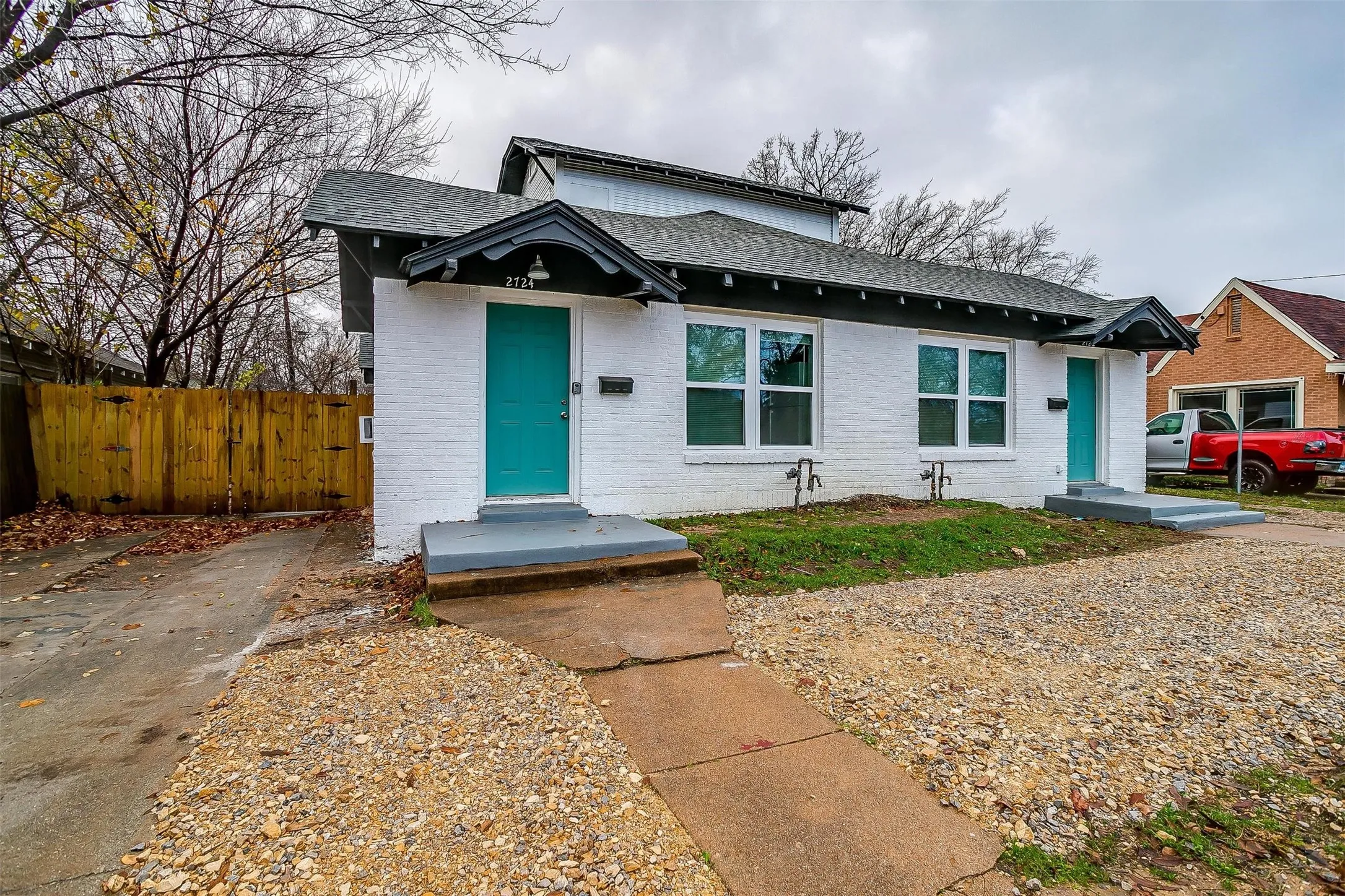 White brick exterior featuring dual covered entryways, gabled rooflines, teal-painted doors, and light-filled windows