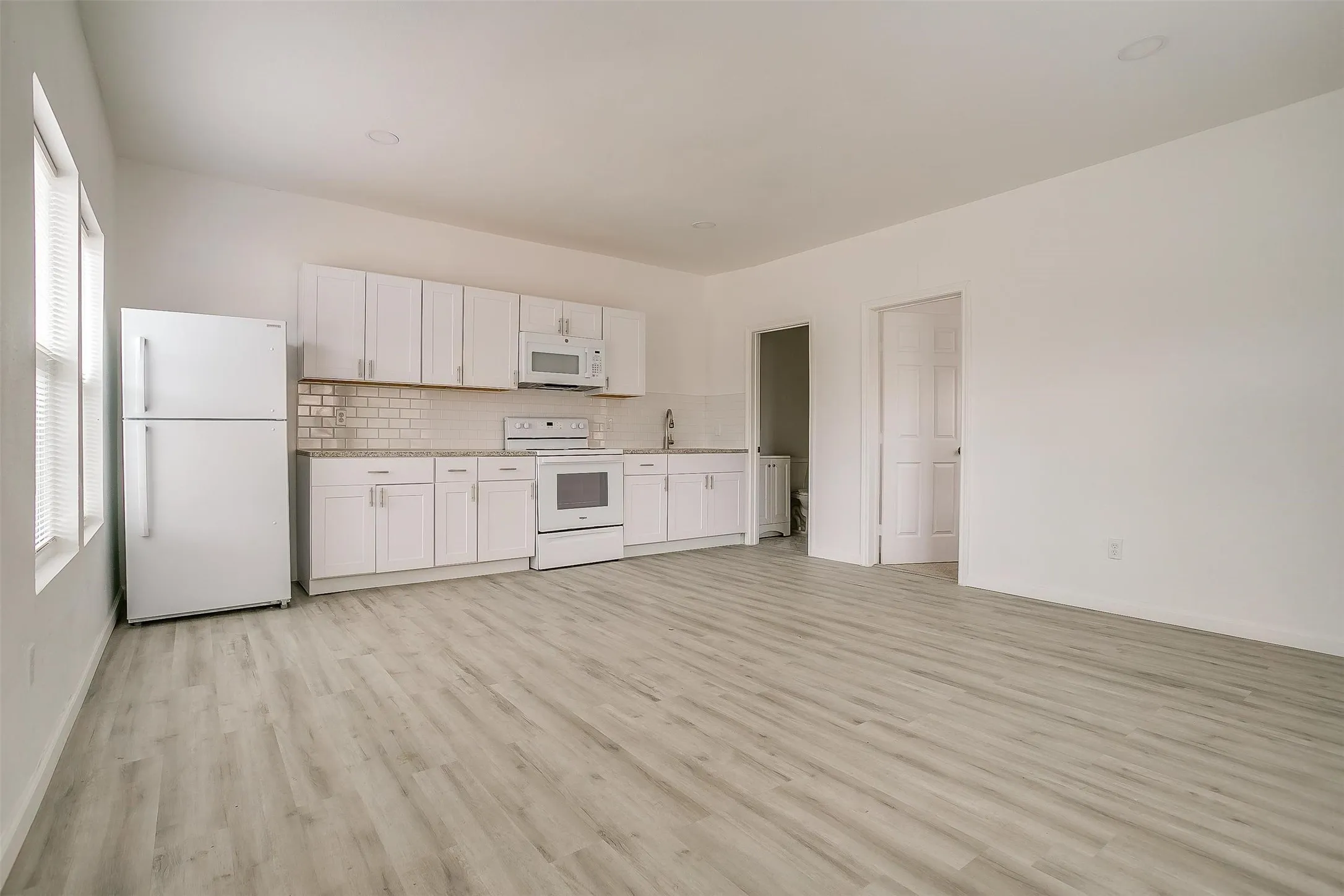 Kitchen featuring white cabinetry, stone-finish countertops, tiled backsplash, and recessed lighting, complemented by wood-finish flooring