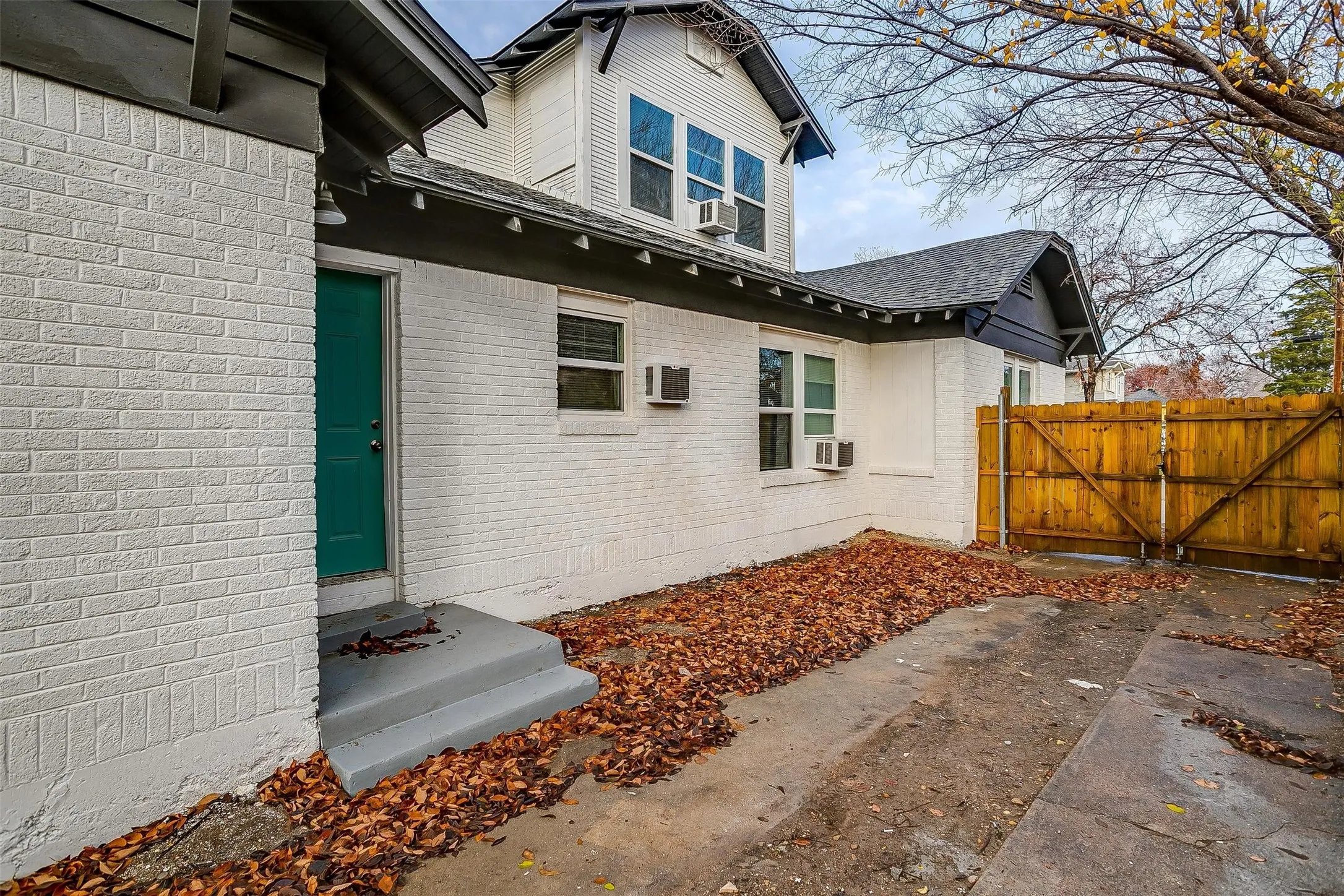 Painted brick exterior, multi-level roofline with gable detail, concrete surface, and wood-panel privacy fencing