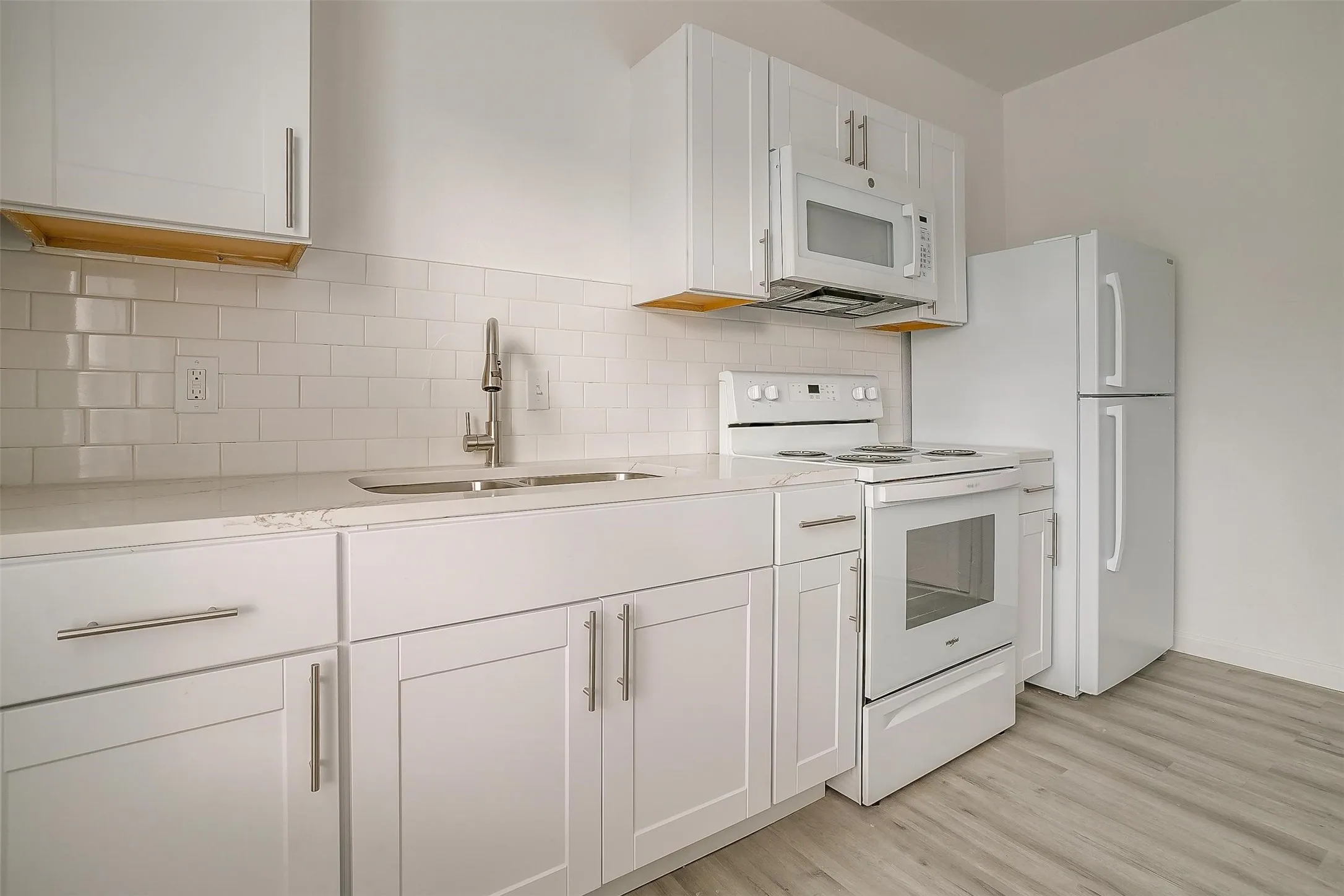 Kitchen featuring white Shaker-style cabinetry, light-toned countertops, subway tile backsplash, stainless steel arched faucet, and wood-finish flooring
