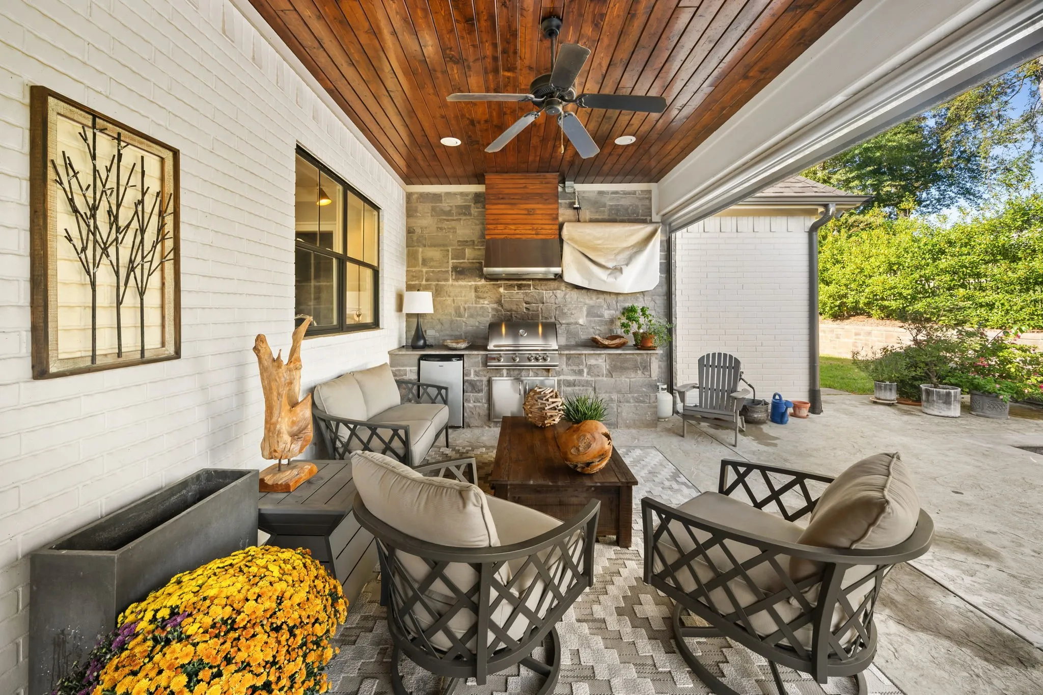 Covered patio featuring a stained wood plank ceiling, stone masonry wall, built-in outdoor kitchen with a stainless steel grill, and integrated recessed lighting