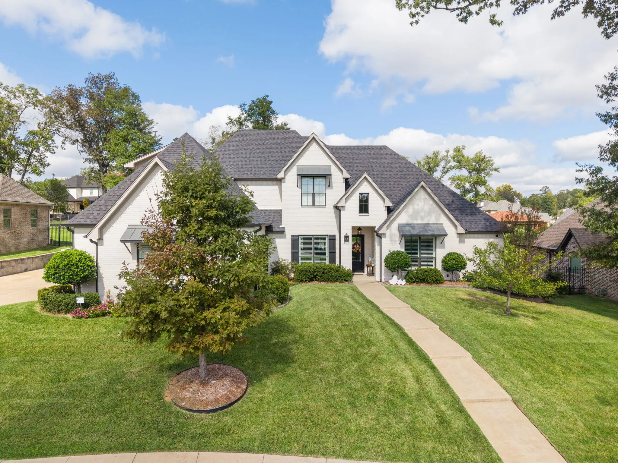 Stucco exterior featuring multi-gabled rooflines, black metal awnings, grid-pattern windows, and a paved walkway