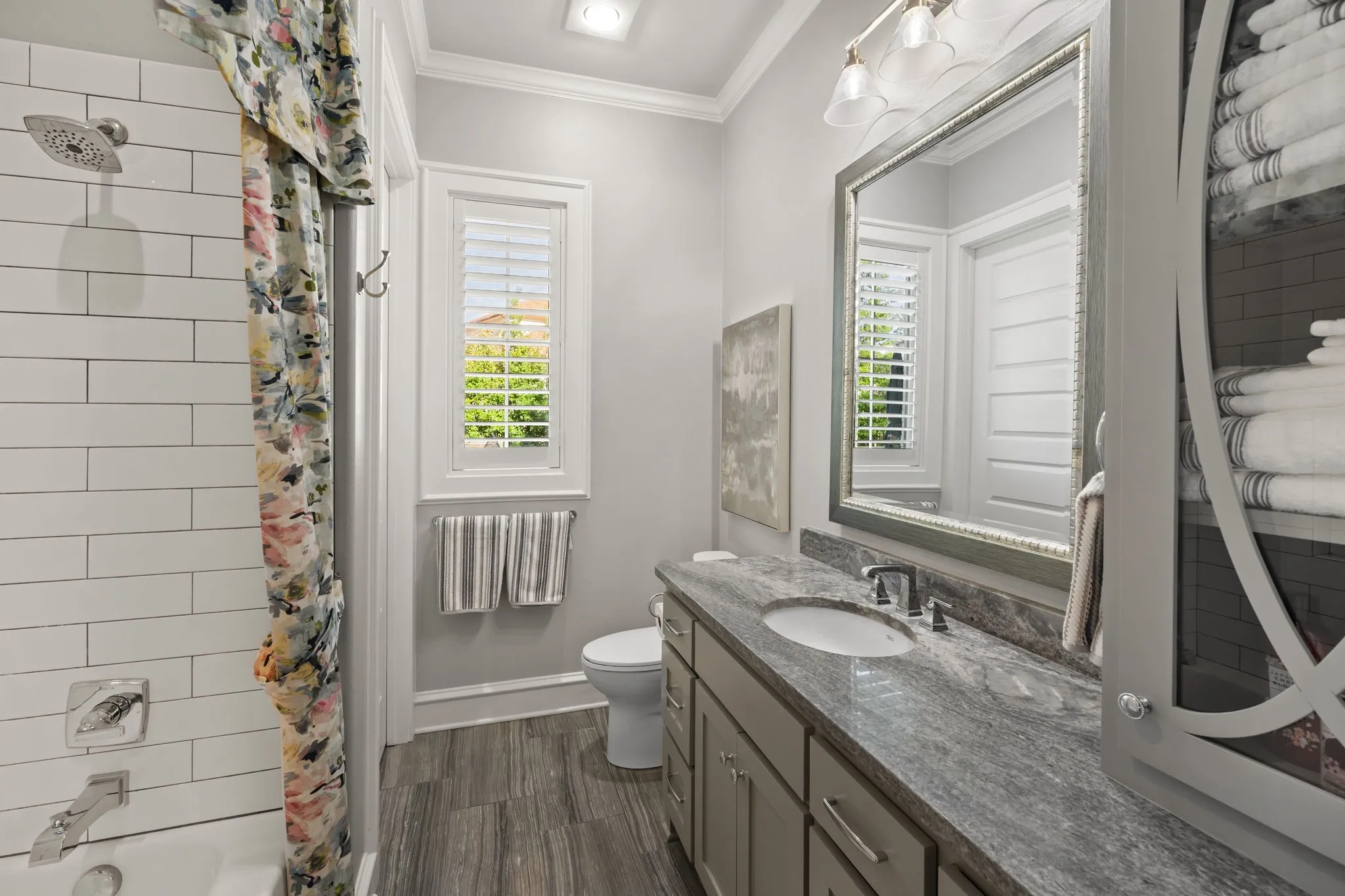 Bathroom featuring a stone-surface vanity with an integrated sink, white subway tile shower surround, interior window shutters, and built-in cabinetry with decorative glass inlay