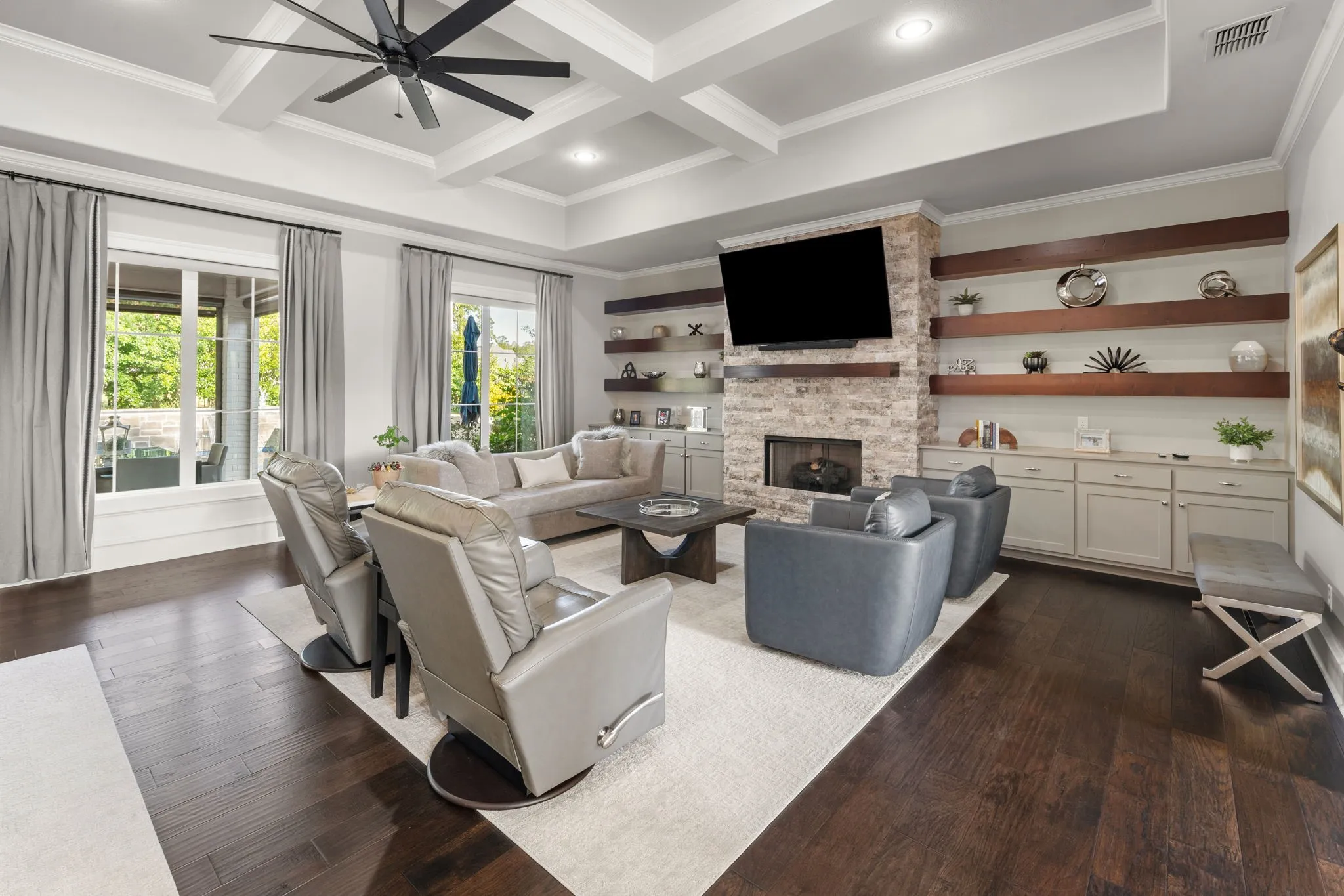 Living area featuring wood-finish flooring, coffered ceiling, stone-surround fireplace, and built-in cabinetry with floating wood shelving