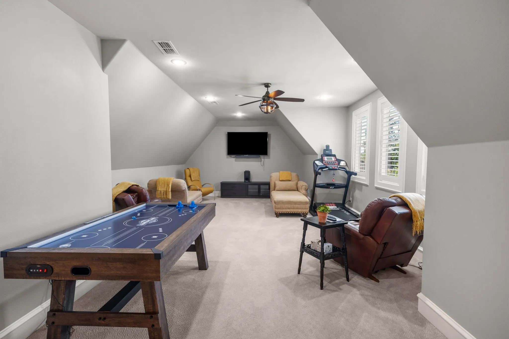Expansive room featuring vaulted ceilings, neutral wall-to-wall carpeting, recessed lighting, a ceiling fan with integrated light fixture, and plantation shutters