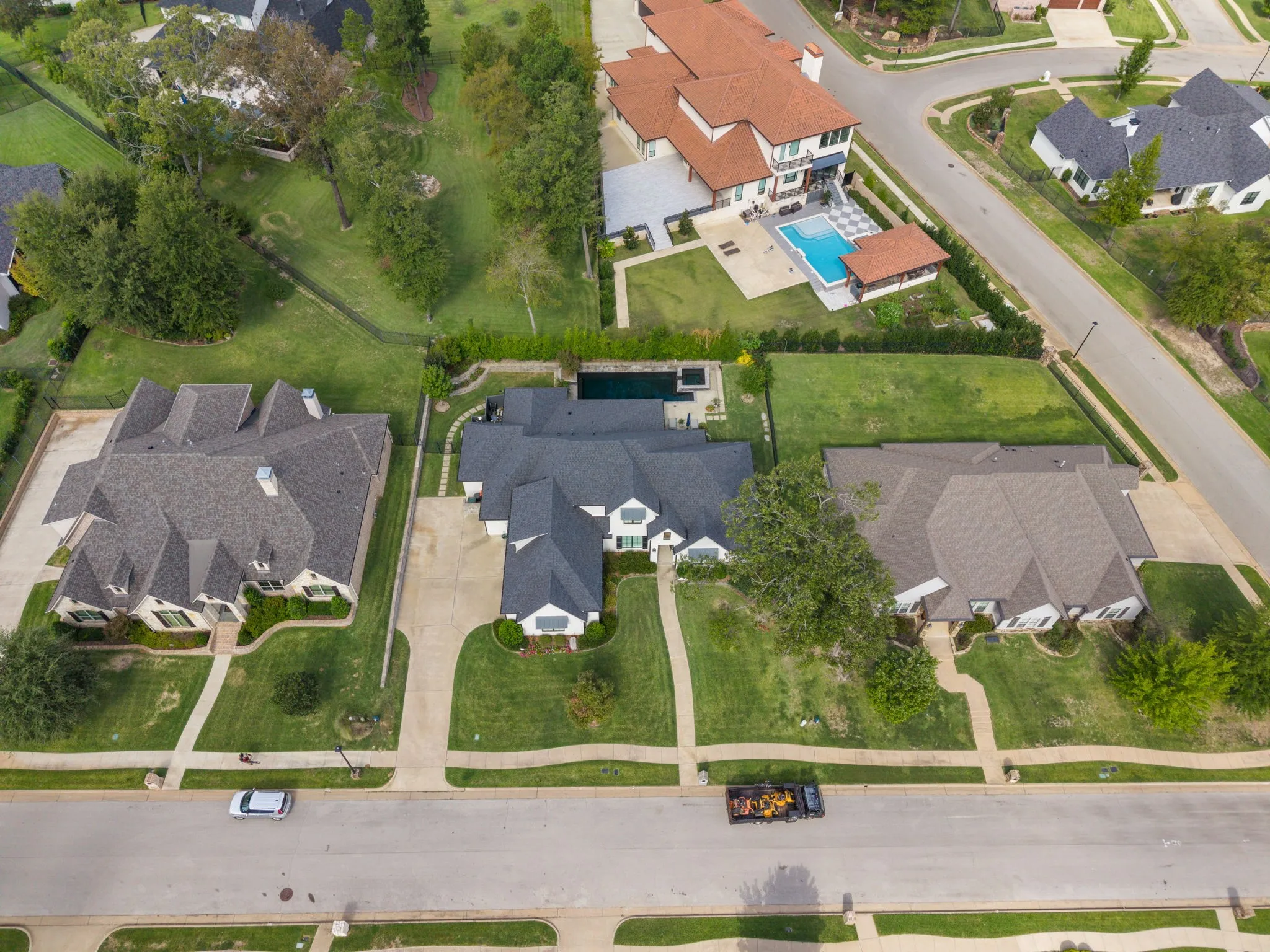 Aerial perspective of a multi-gabled residence featuring a dark shingle roof, concrete driveway, stone-accented exterior, and a private rear swimming pool