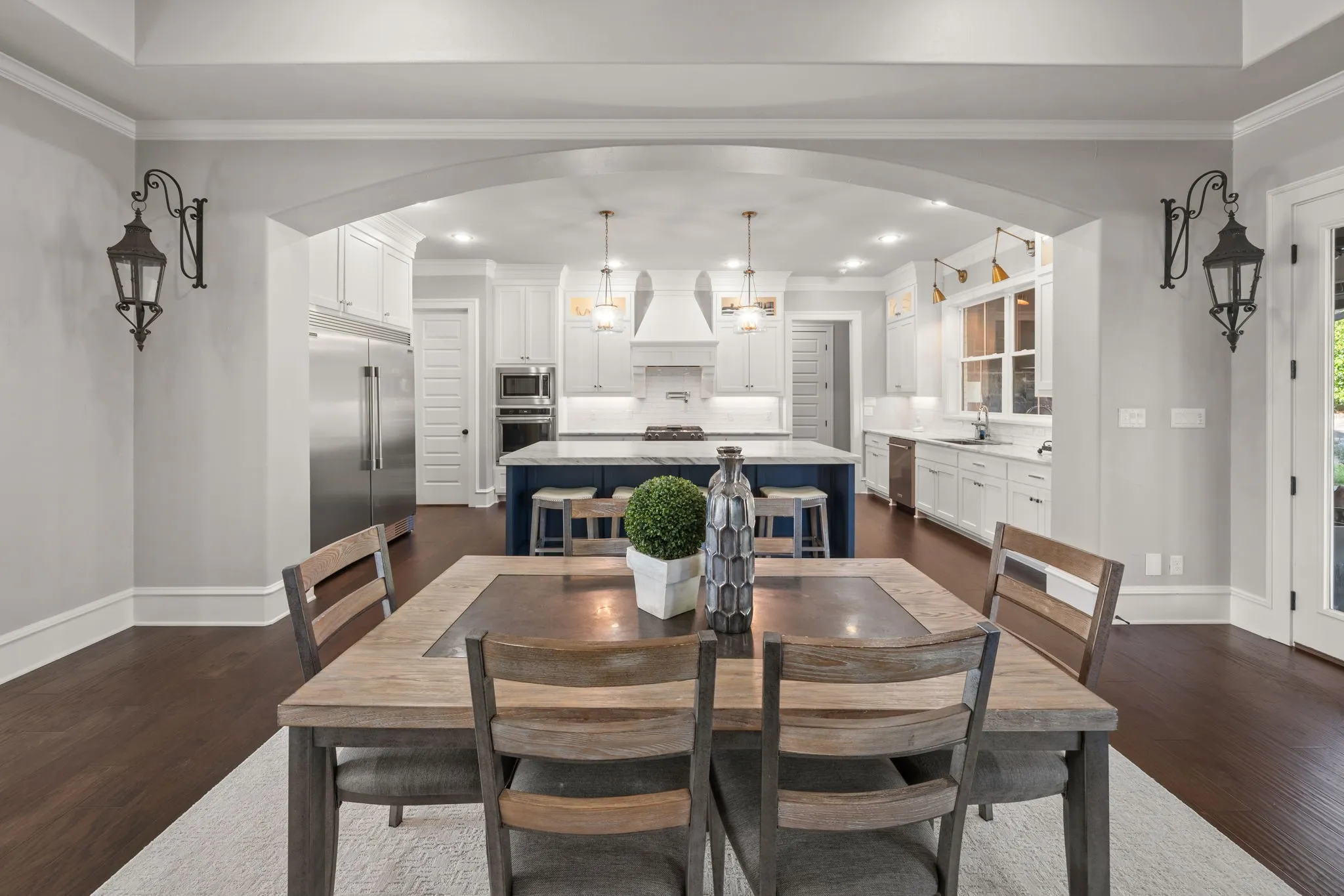Kitchen area featuring an oversized central island with a contrasting base, white shaker-style cabinetry, stainless steel appliances, recessed ceiling lighting, and dark wood-finish flooring