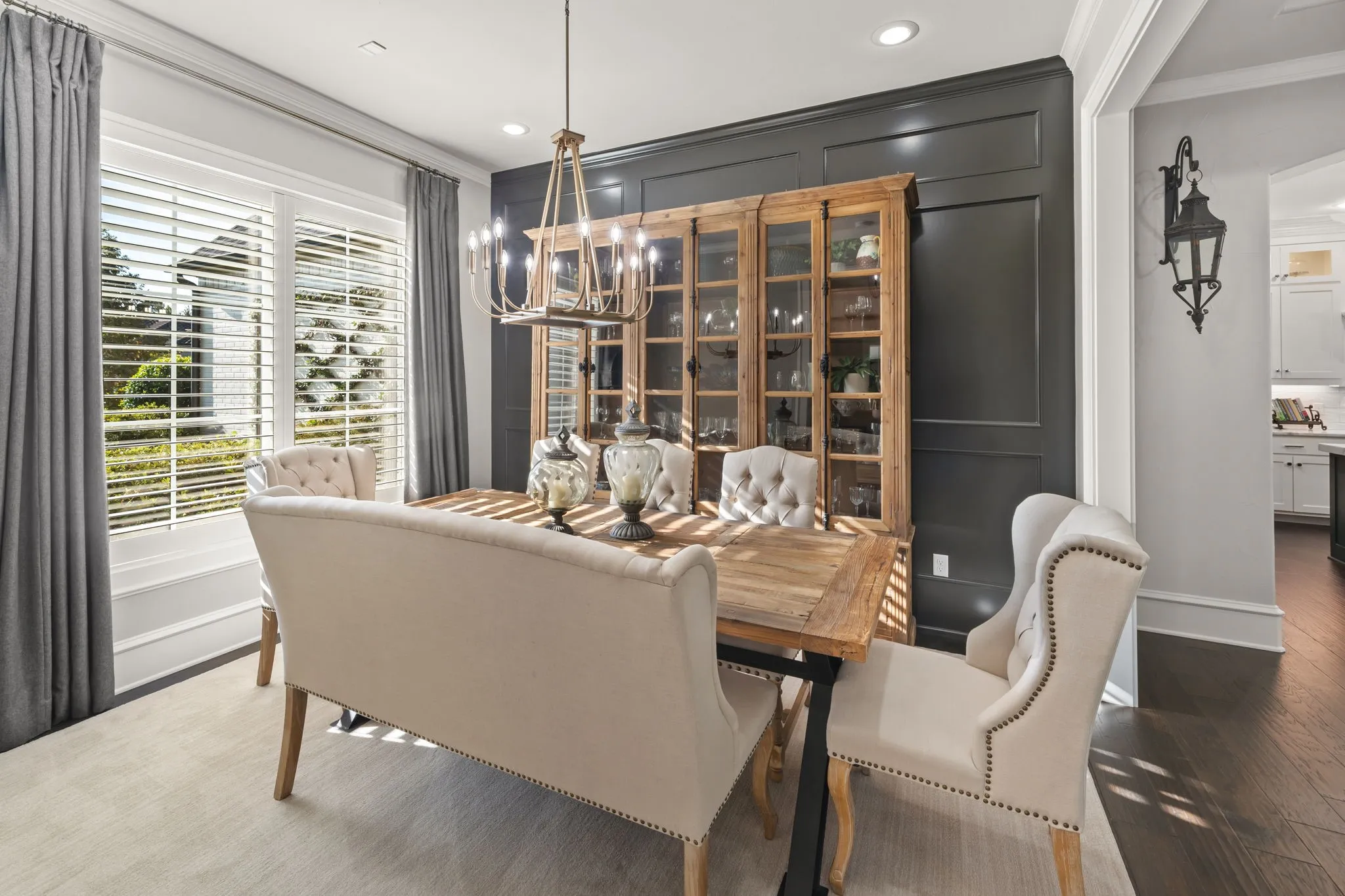 Dining room featuring dark wood-finish flooring, custom-paneled accent wall, plantation shutters, recessed lighting, and a multi-tiered chandelier