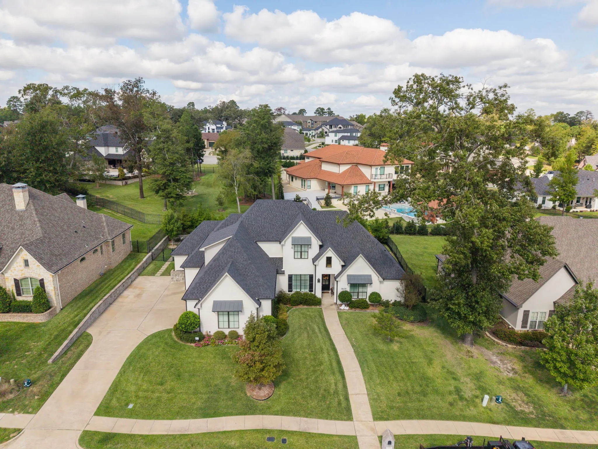 Multi-gabled roofline with shingled exterior, light-toned masonry facade, decorative metal window awnings, and multi-car concrete driveway