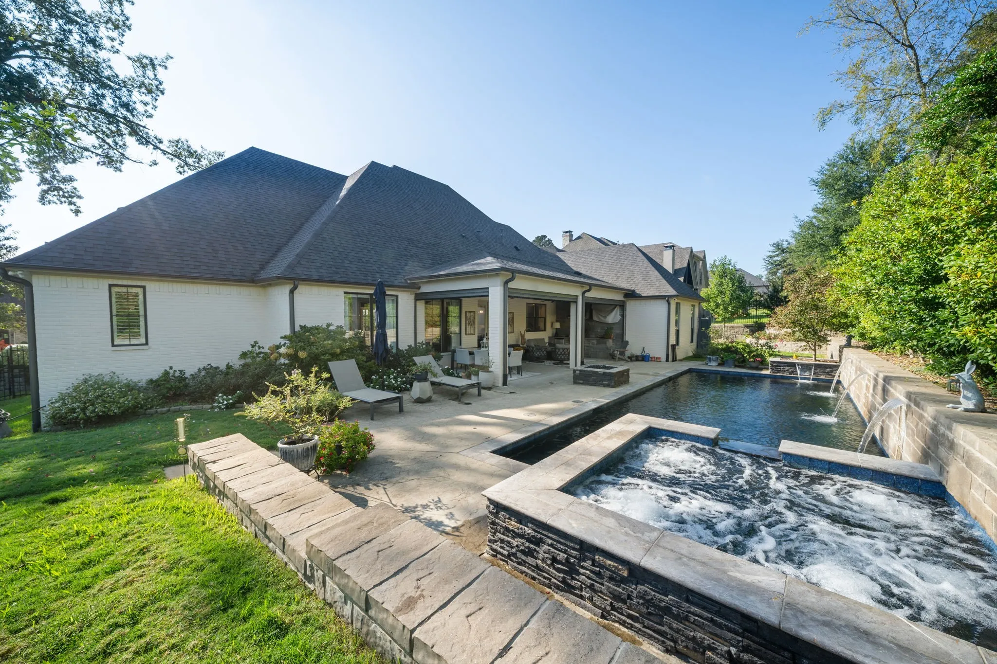 Backyard featuring a covered patio, rectangular swimming pool with integrated water features, stone-finish spa, and tiered natural stone retaining walls