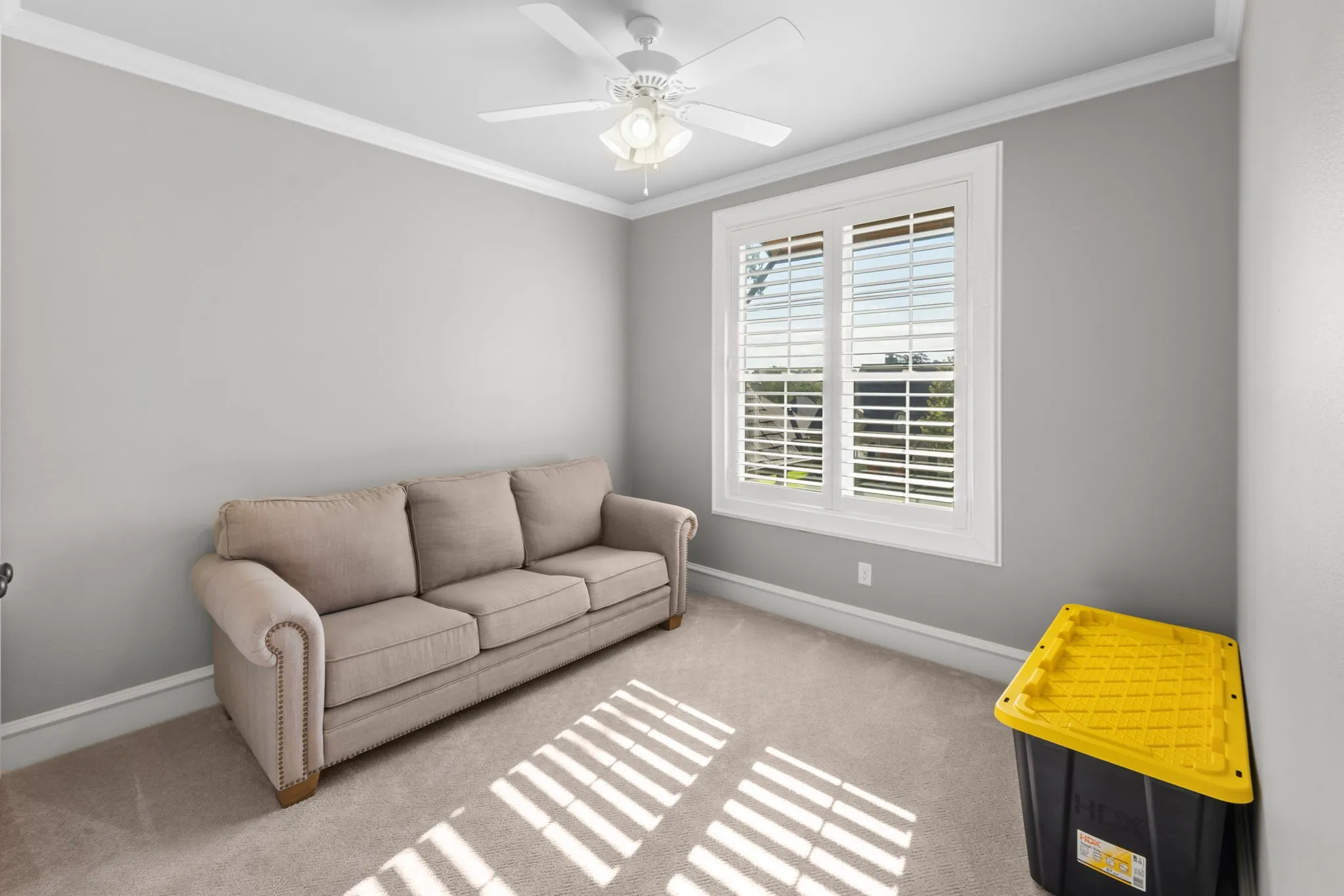 Neutral-toned room featuring plush carpeting, a white ceiling fan with integrated lighting, and plantation-style window shutters