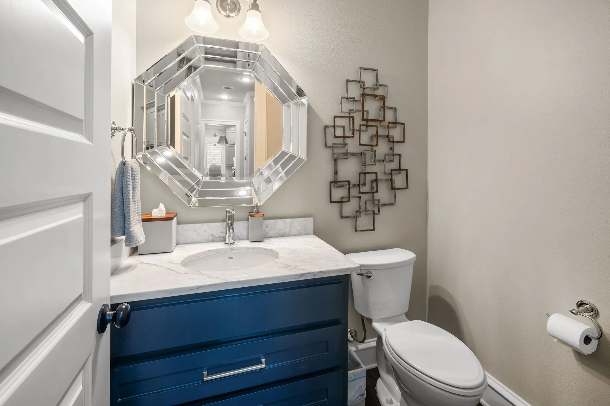 Navy blue vanity with stone countertop, integrated sink, and chrome fixtures, paired with a multi-faceted octagonal mirror and dual-light wall sconce