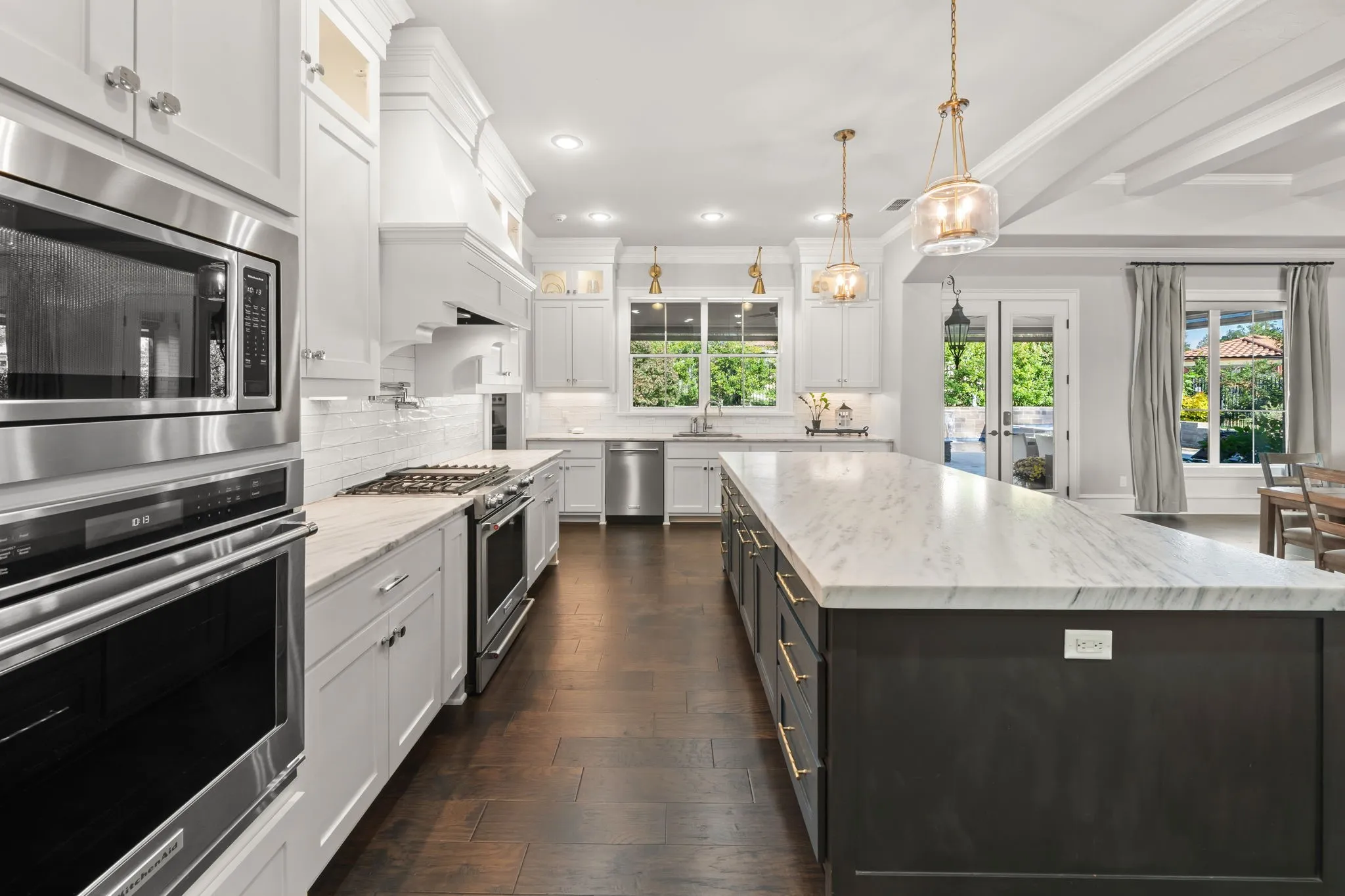 Gourmet kitchen featuring a large central island with stone-finish countertops, custom cabinetry with brushed gold hardware, stainless steel appliances, and dark wood-finish flooring