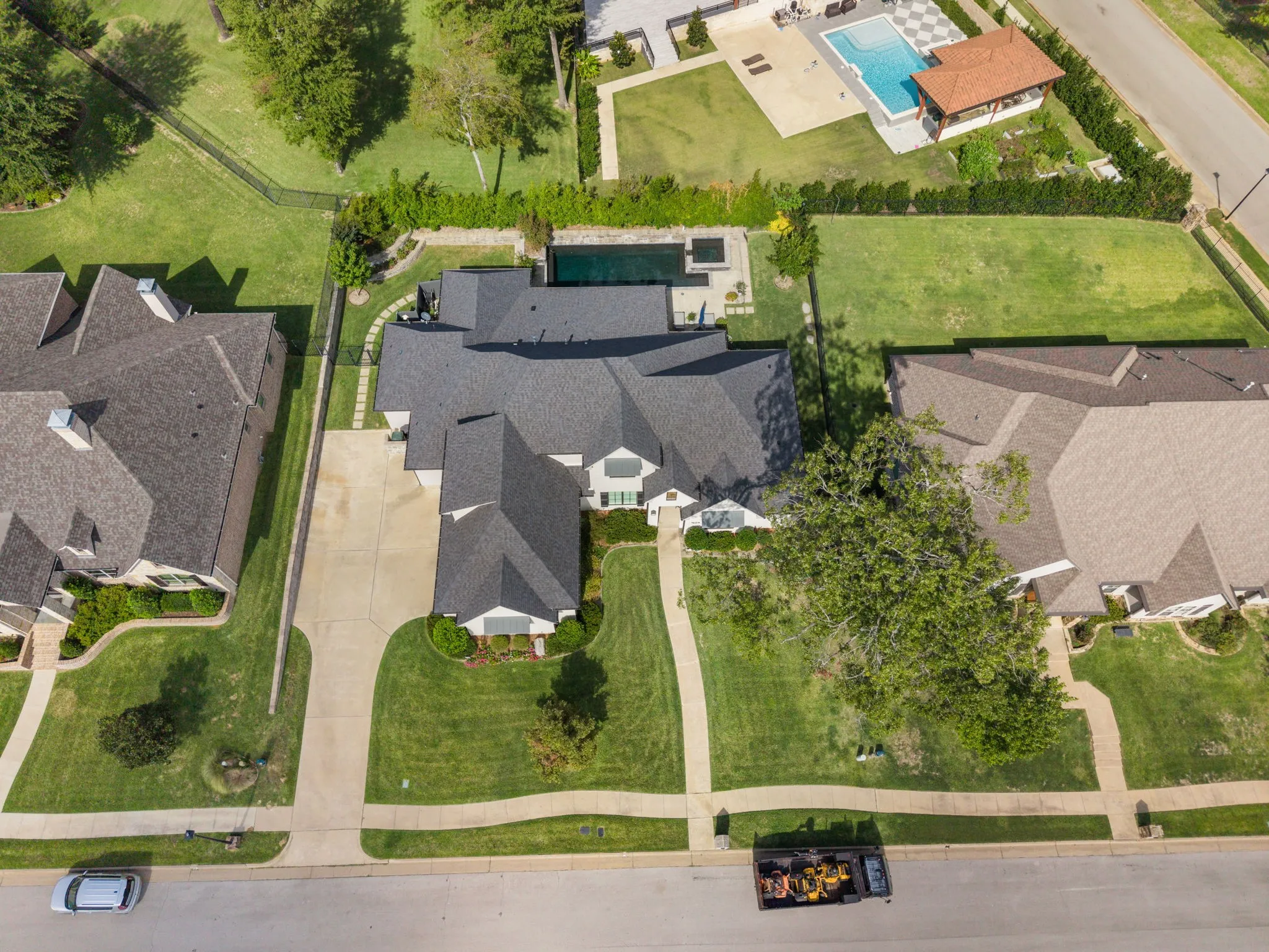 Aerial perspective featuring a multi-gabled roofline, concrete driveway, stone-paved walkway, and a rectangular swimming pool with an integrated spa