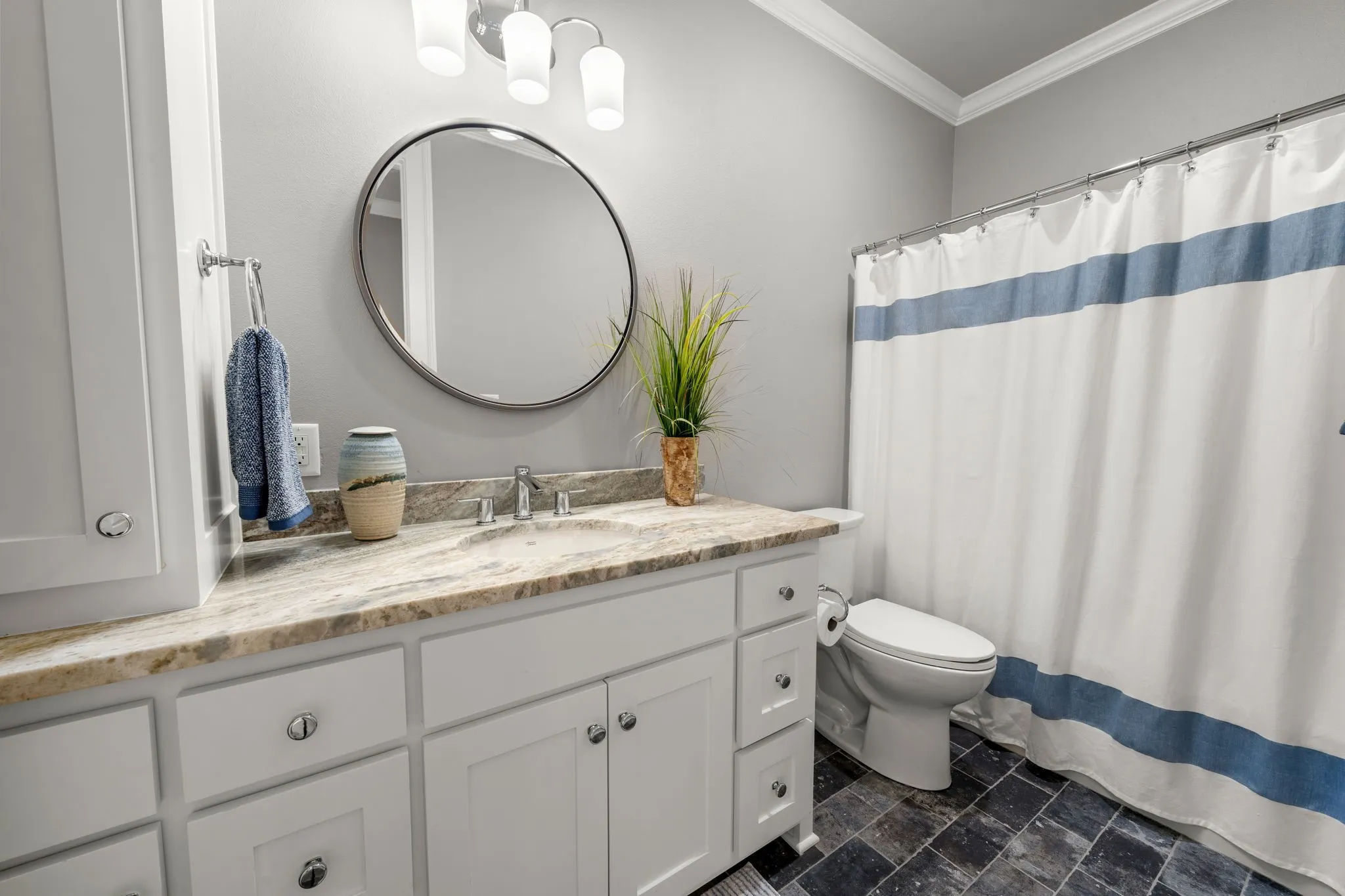 Bathroom featuring a white shaker-style vanity with stone-patterned countertop, integrated basin, round mirror, and tile flooring