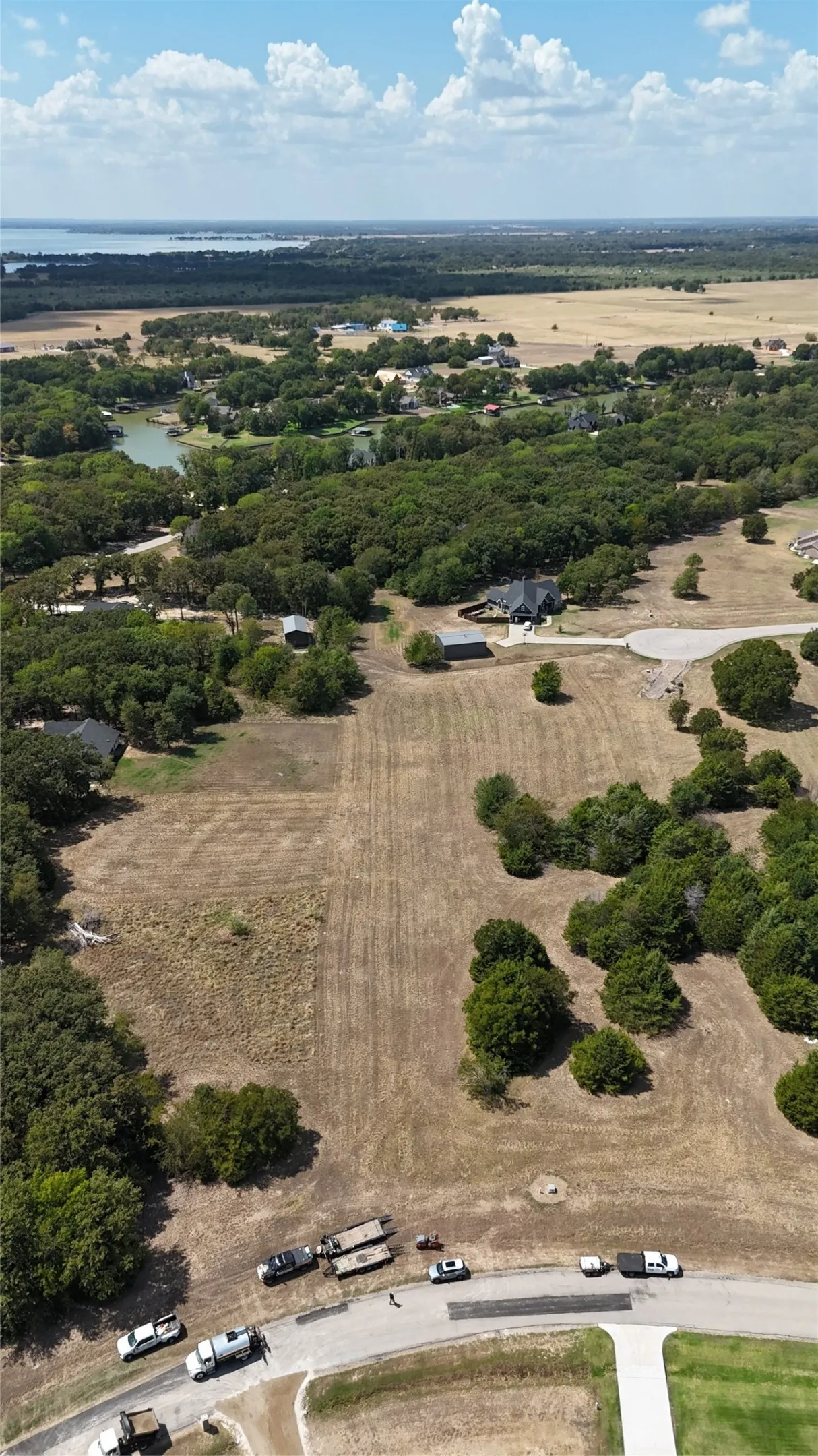 Aerial view of expansive acreage featuring mature trees, open clearing, paved road access, and water in the distance