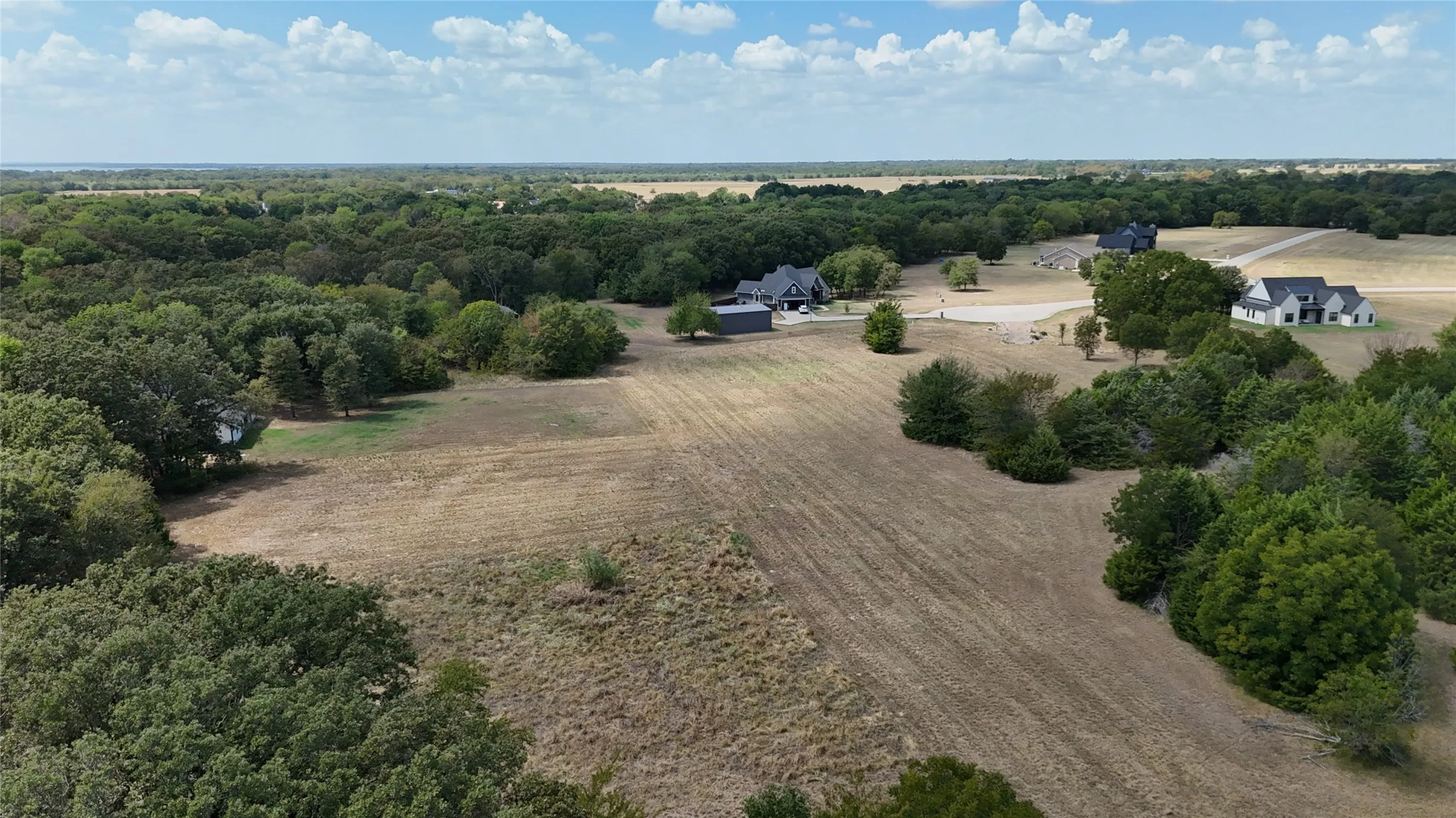 Expansive acreage featuring cleared pasture land, dense mature tree clusters, and gravel access roads