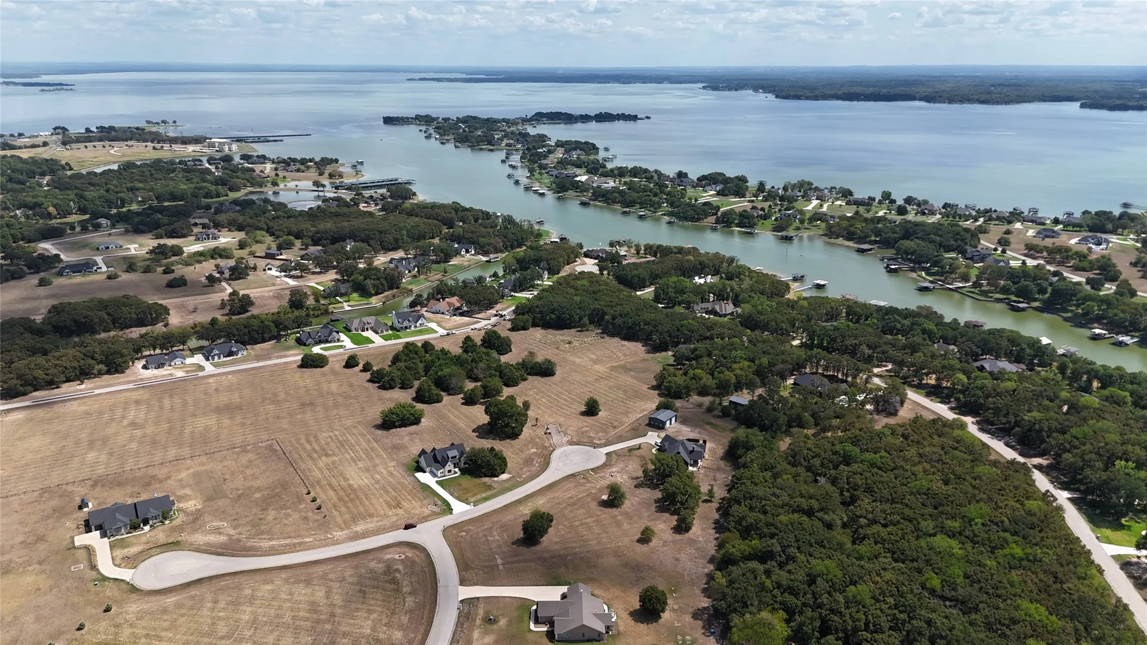 Aerial perspective showcasing expansive acreage, mature tree clusters, paved cul-de-sac streets, and extensive waterfront shoreline