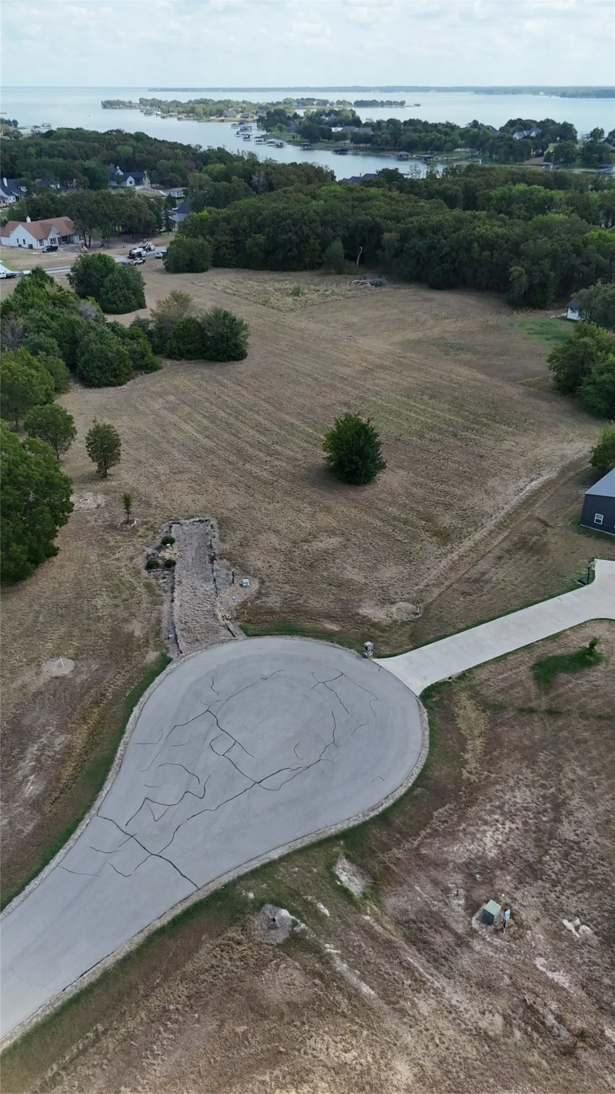 Expansive corner lot featuring a paved cul-de-sac entrance, mature trees, and direct exposure to a large body of water