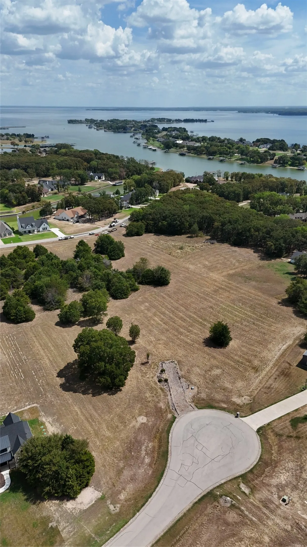 Expansive unimproved acreage featuring mature tree clusters, paved cul-de-sac street access, and water frontage
