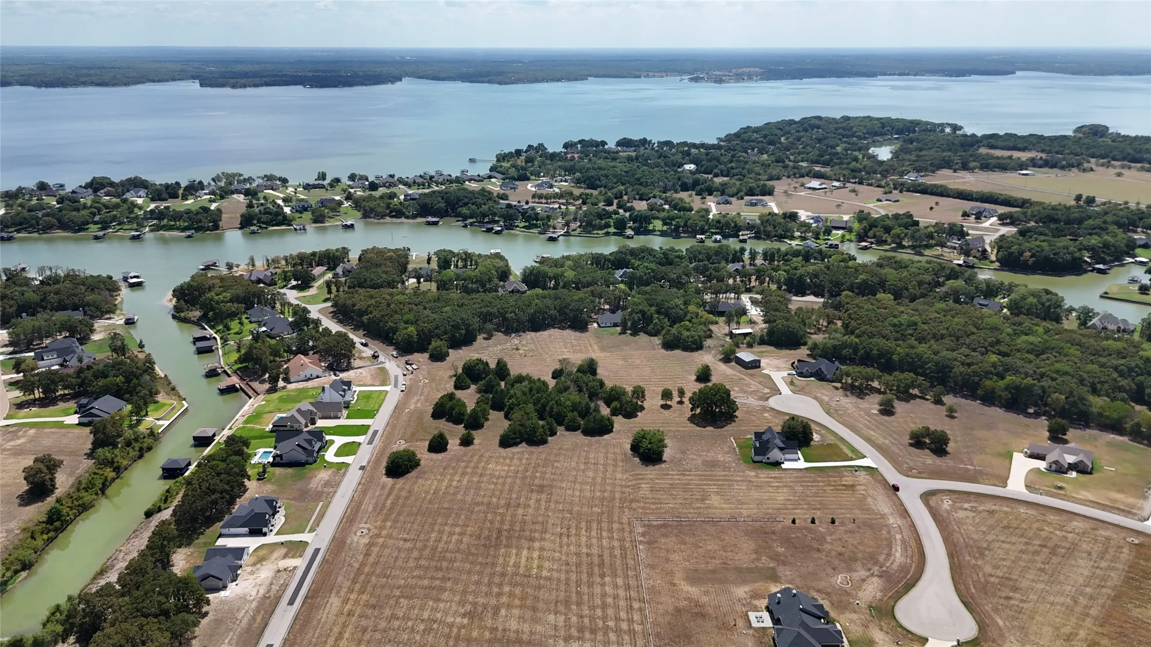 Aerial perspective of land featuring water frontage, mature trees, and paved roadway infrastructure