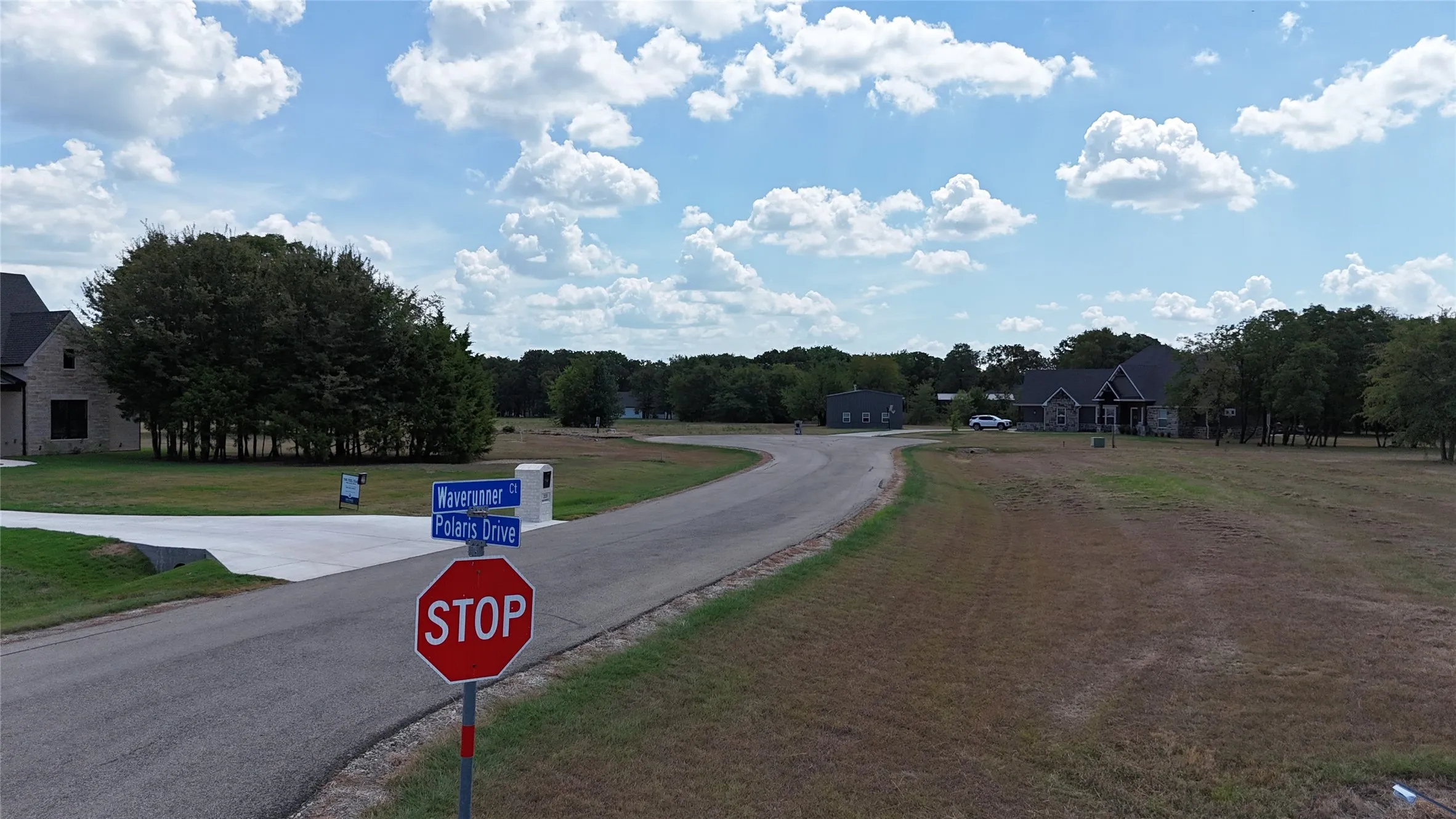 Corner lot featuring paved roads, concrete driveway, and mature trees